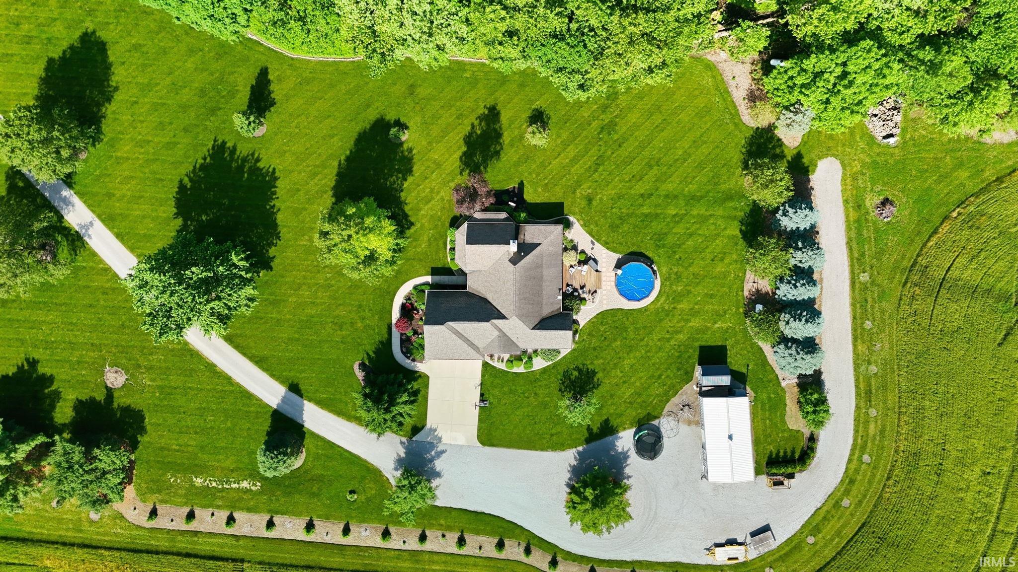 Expansive property featuring a circular driveway, a large in-ground pool with surrounding patio, a separate outbuilding, a secondary gravel driveway, and mature landscaping throughout