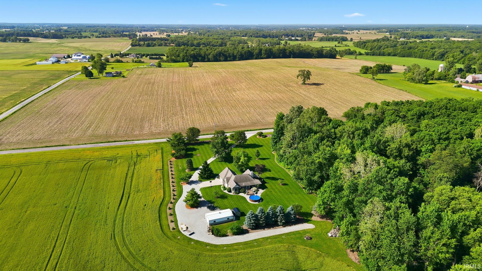 Aerial property view featuring a manicured lawn, an in-ground pool, and mature trees