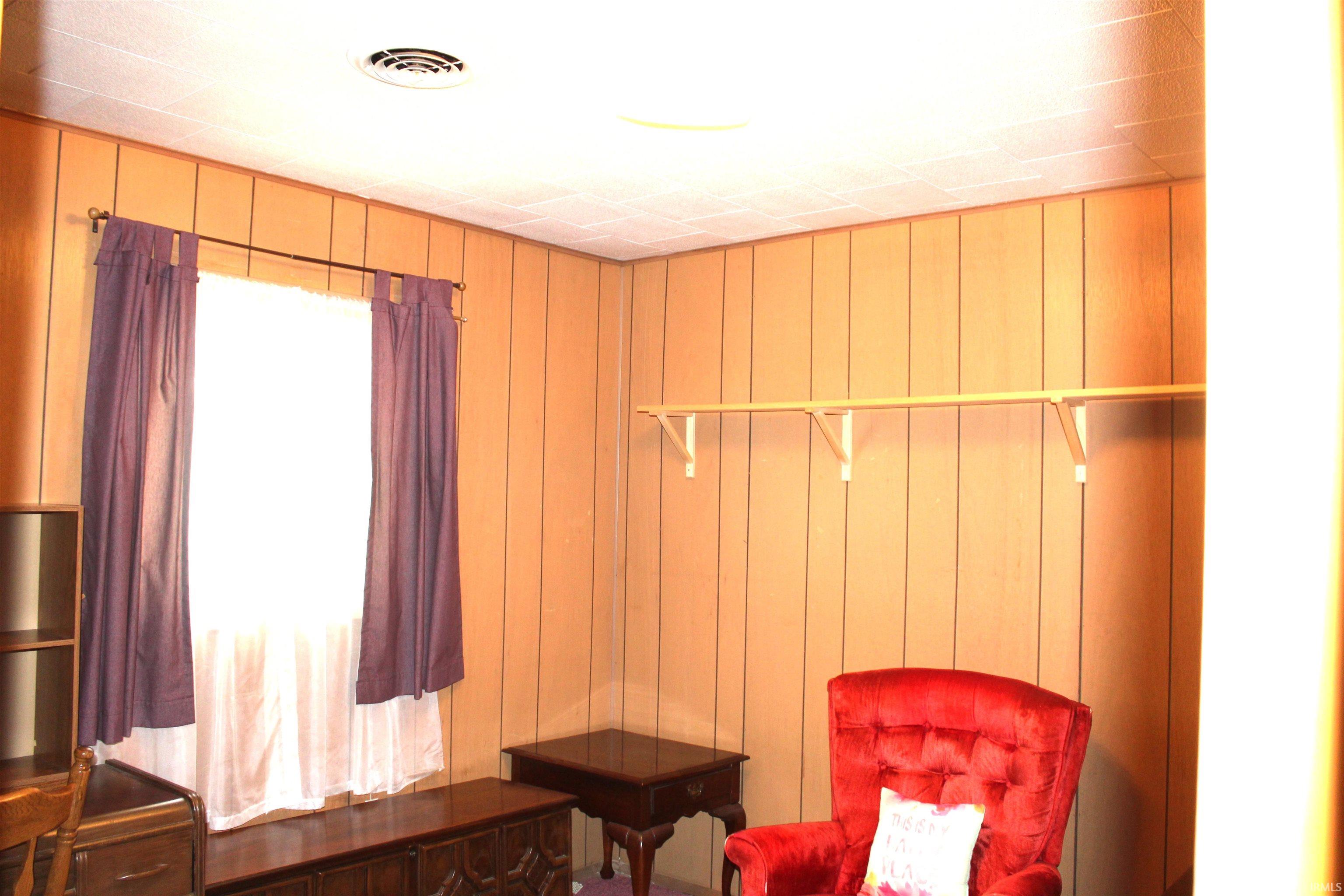 Room with vertical wood paneling, a large window, a ceiling vent, and a built-in hanging rod with shelving brackets