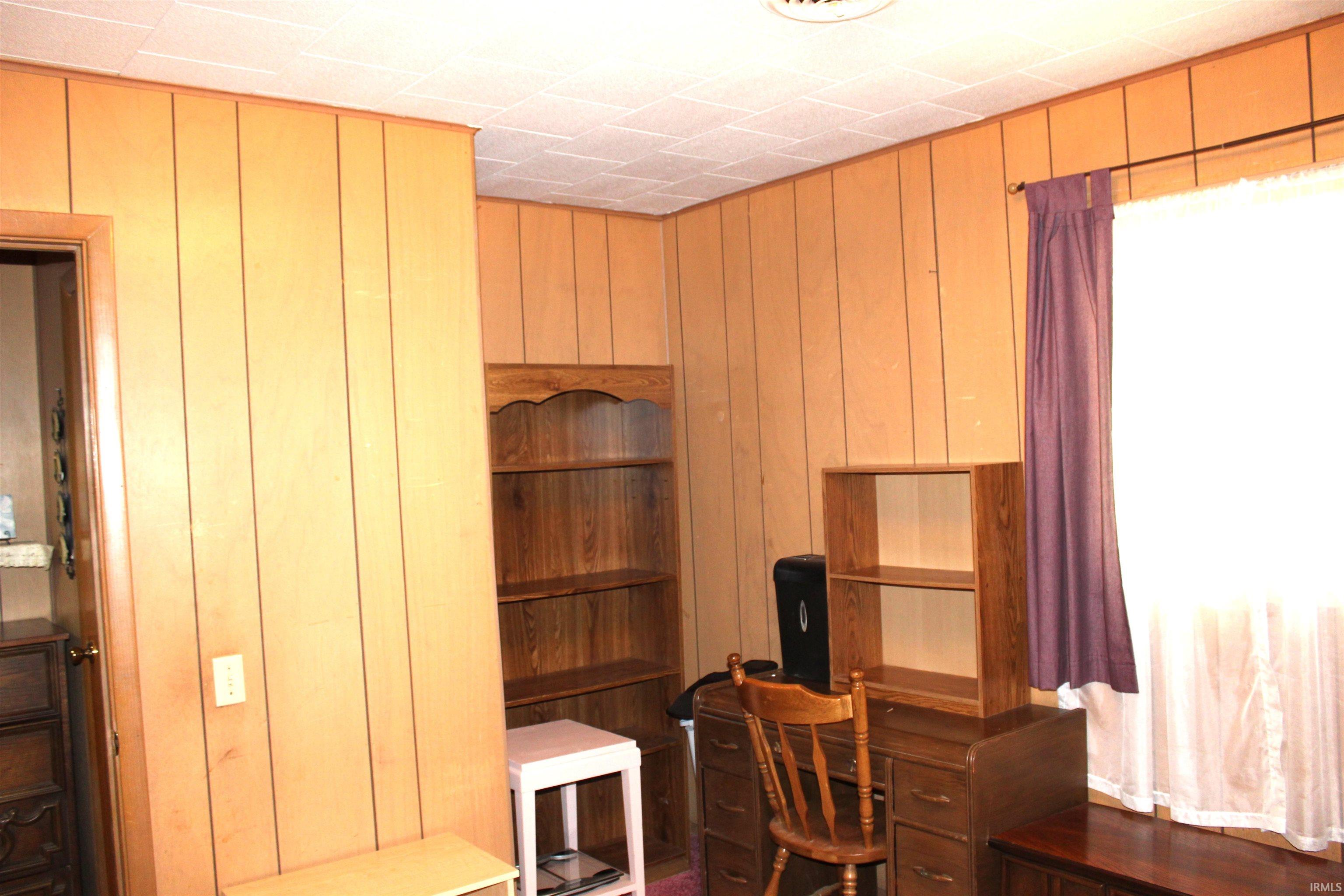 Wood-paneled room featuring a window with privacy sheers and a decorative valance