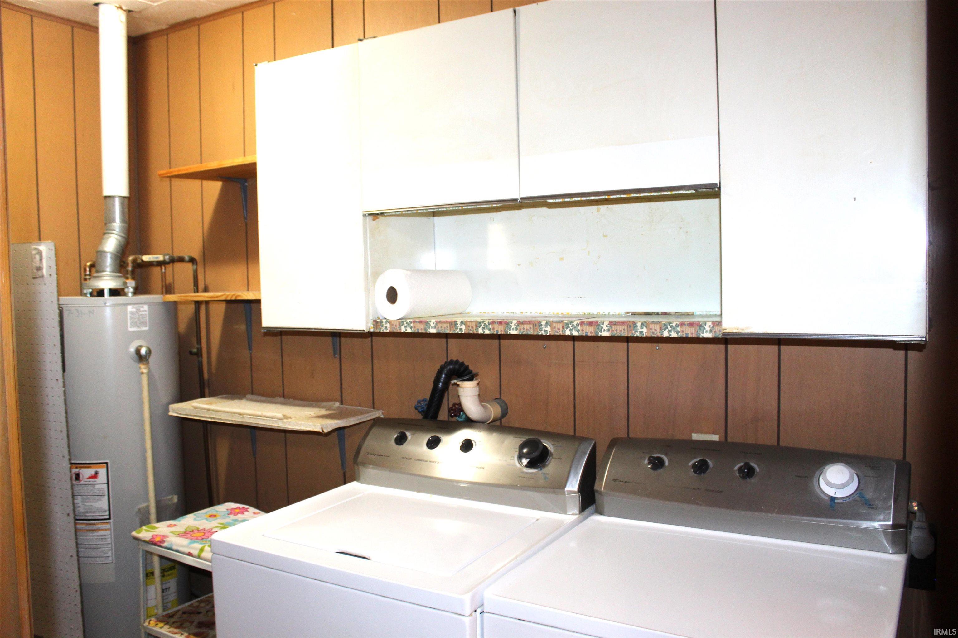 Utility space featuring wood paneling, a water heater, and a floating shelf