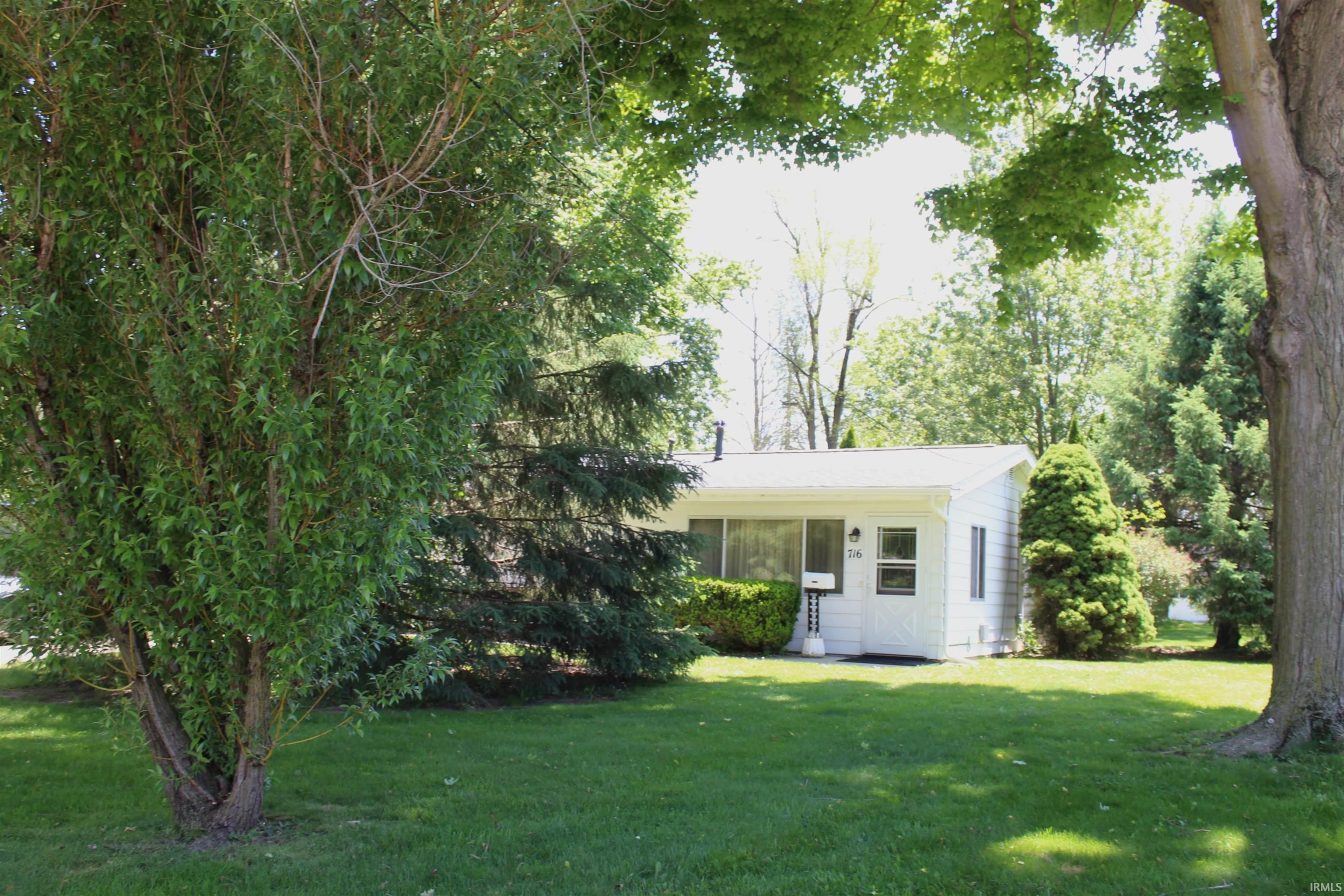White single-story residence featuring a front yard with mature trees and established landscaping