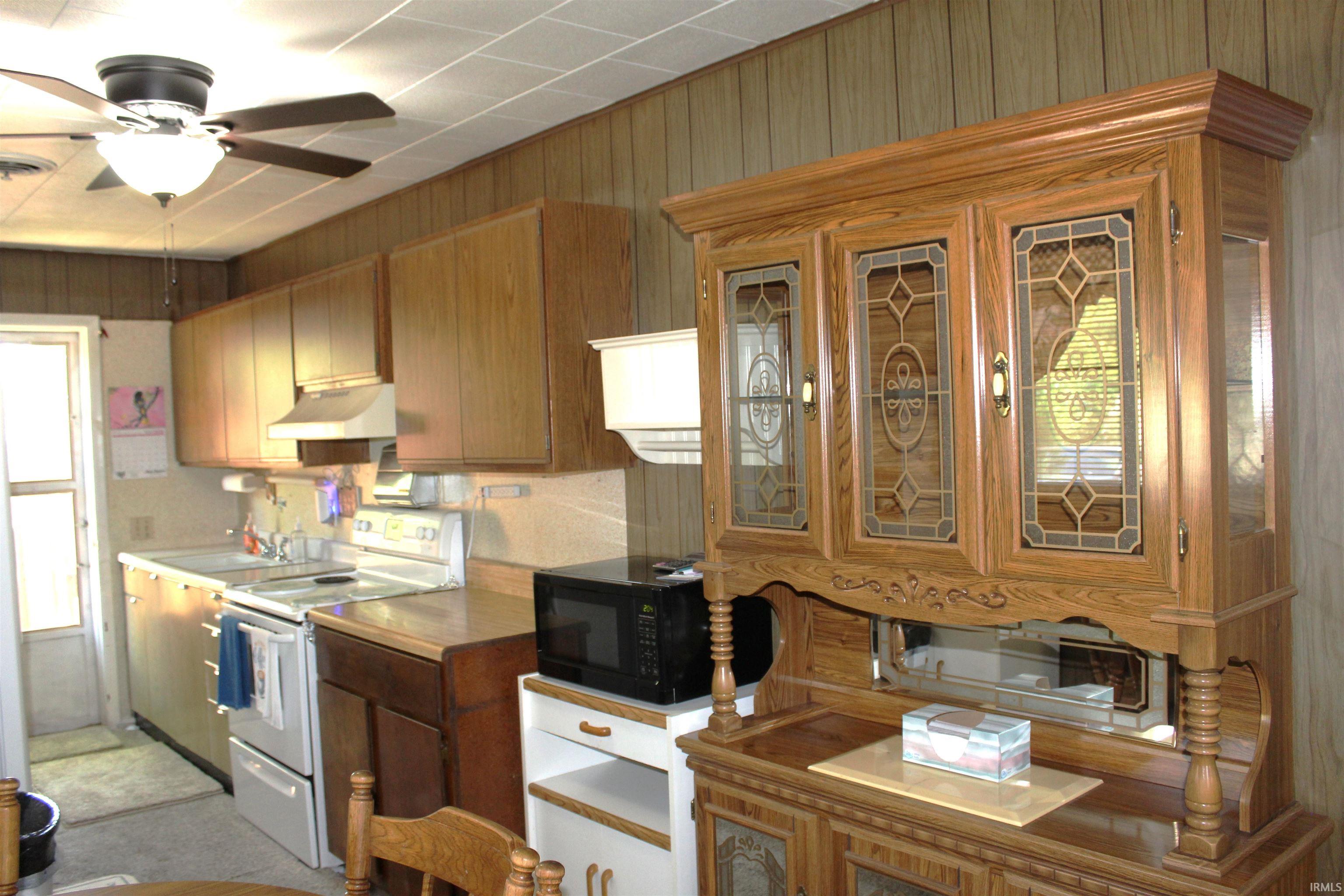 Kitchen featuring wood-paneled walls, white ceiling panels, and a ceiling fan with light fixture