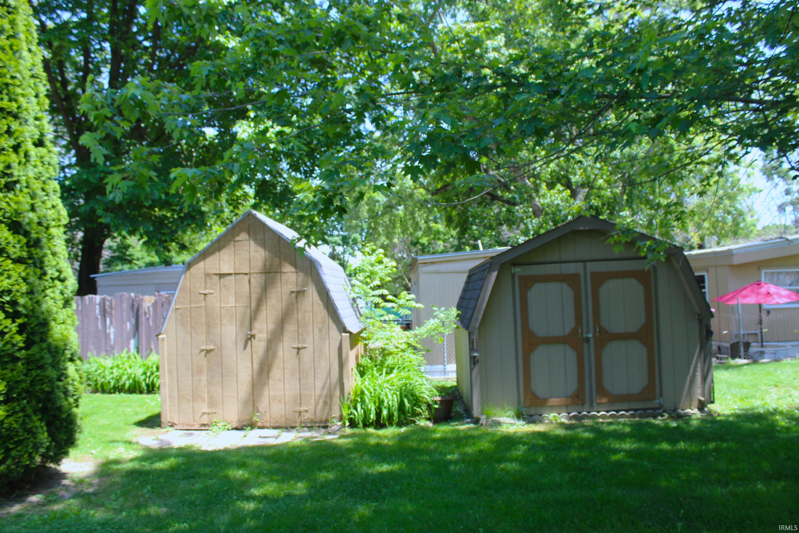 Two backyard storage sheds on a manicured lawn, featuring gambrel roofs and wood-panel siding