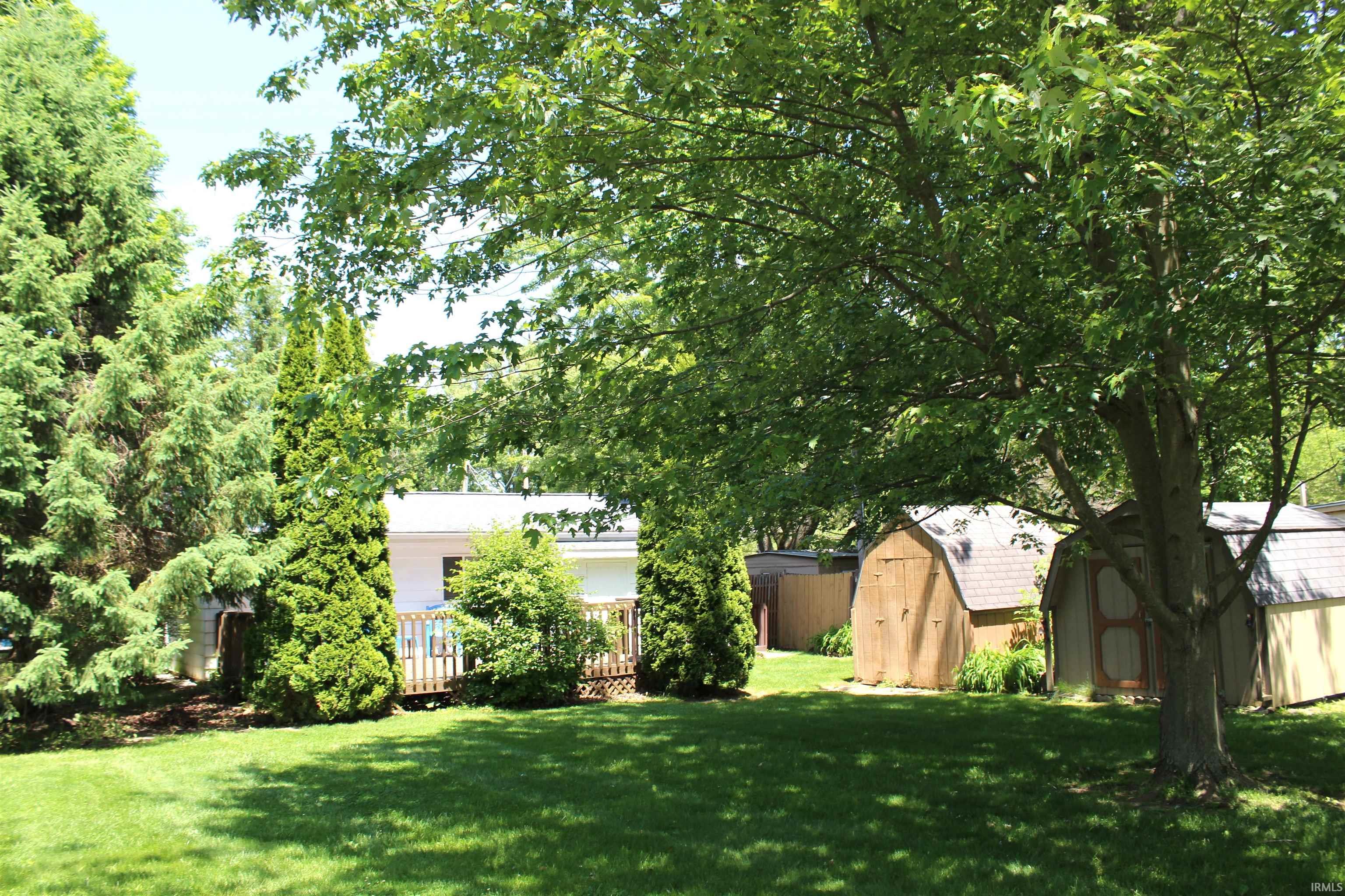 Spacious backyard featuring a lush lawn, mature trees, and a wooden deck