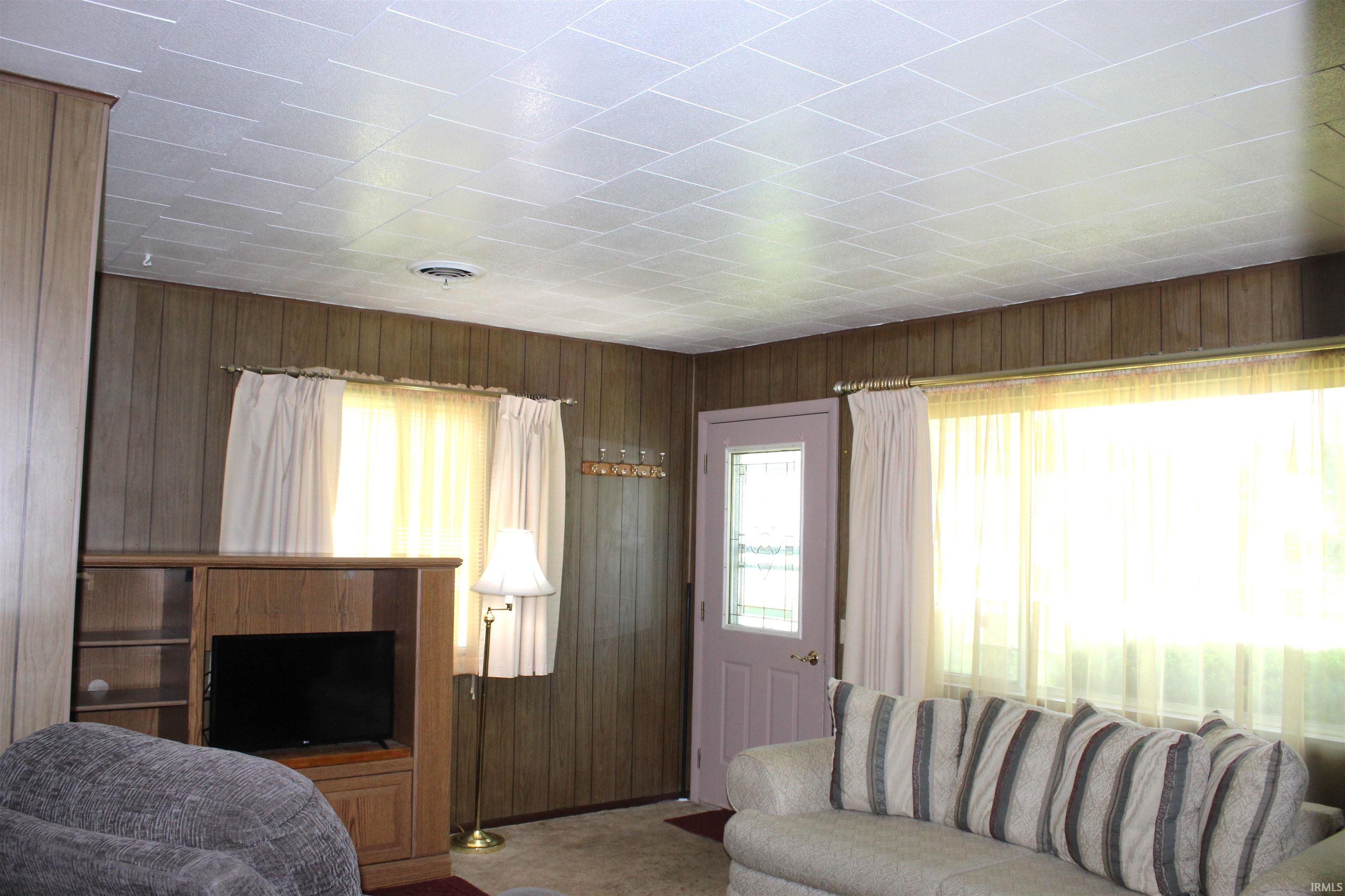 Living space featuring wood-paneled walls and a white grid ceiling