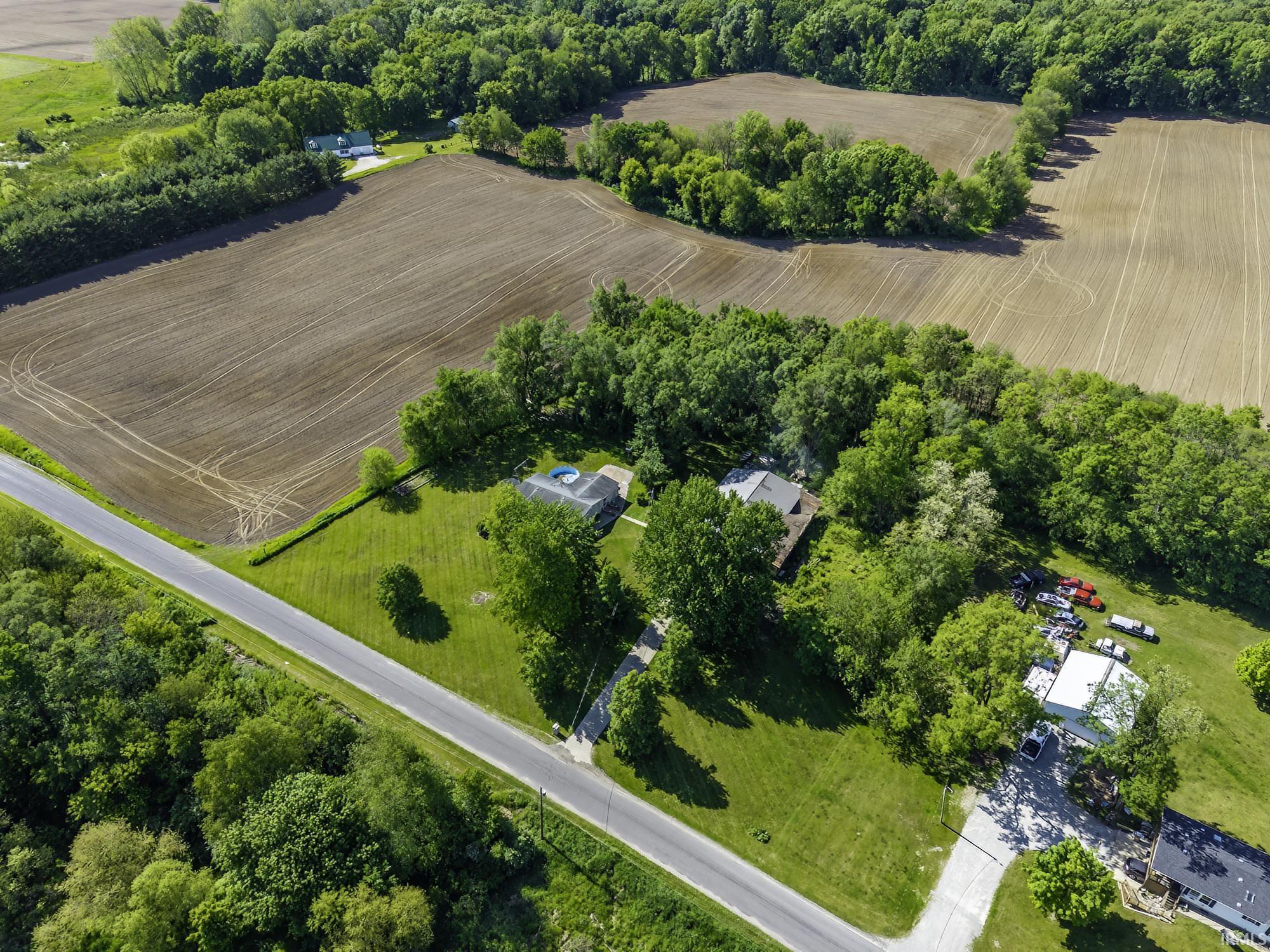 Rural property featuring extensive green spaces, mature tree coverage, and a paved road frontage