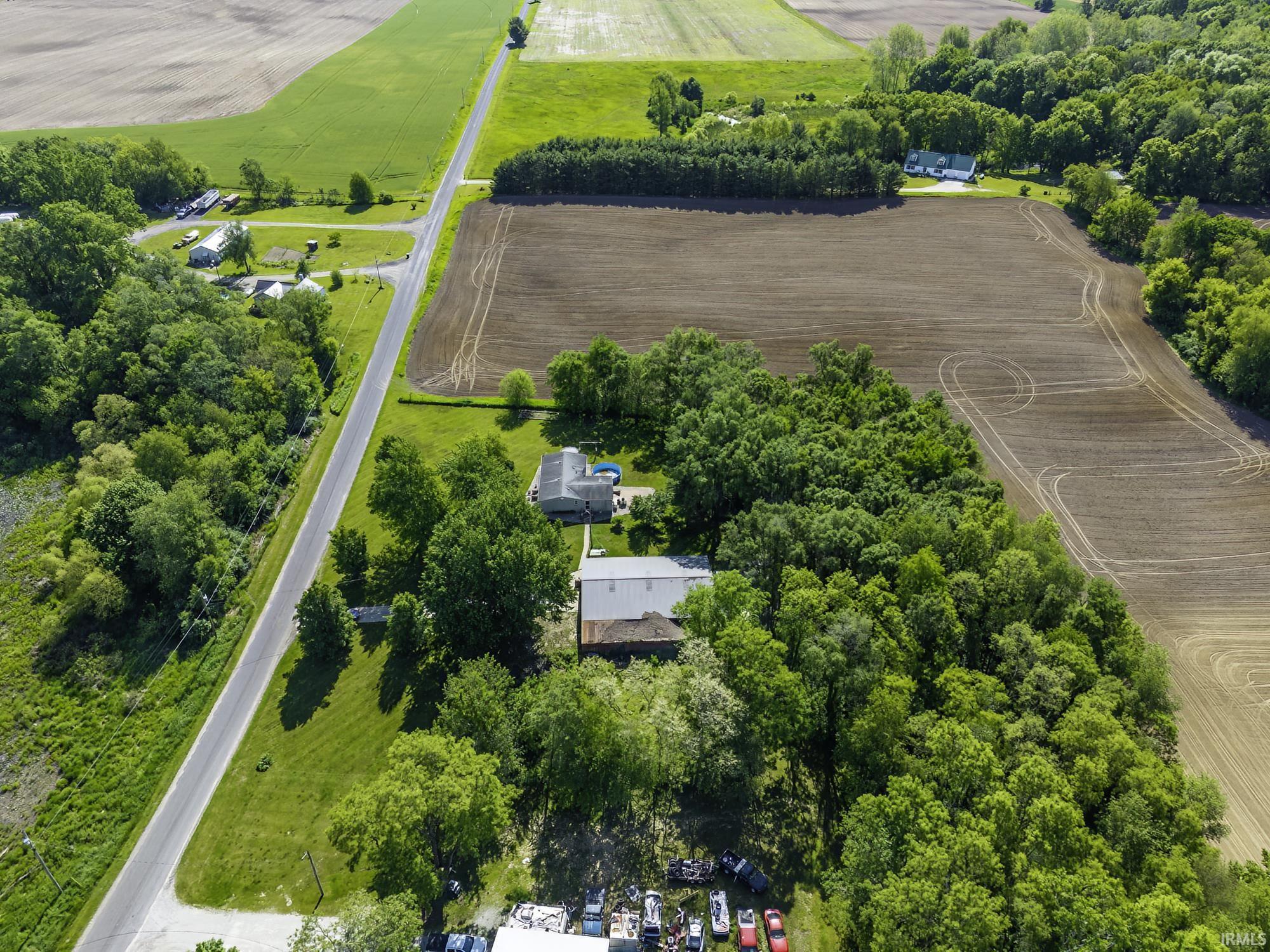Aerial perspective featuring a two-lane road, multiple residential structures, and extensive agricultural fields