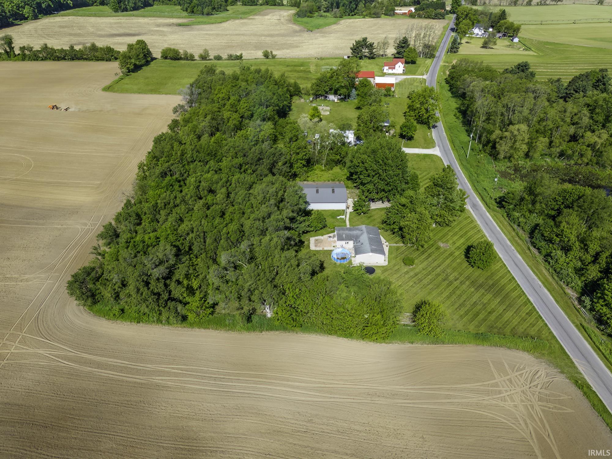Expansive property with a single-story residence featuring a gray roof, surrounded by mature trees and manicured lawns
