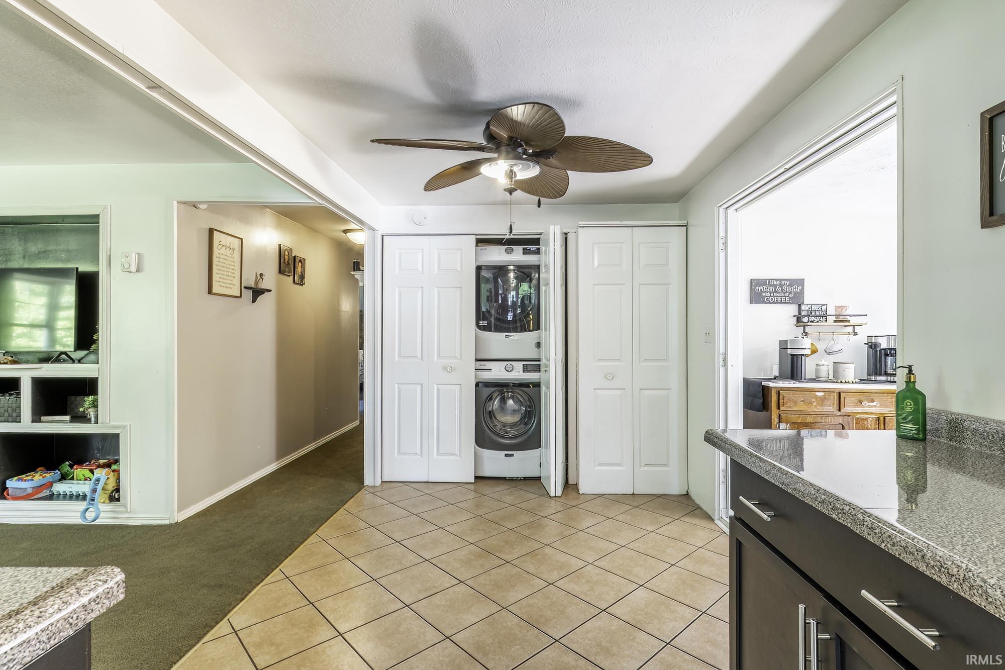 Tile flooring extending into the kitchen area with dark cabinetry, granite-style countertops, and a ceiling fan