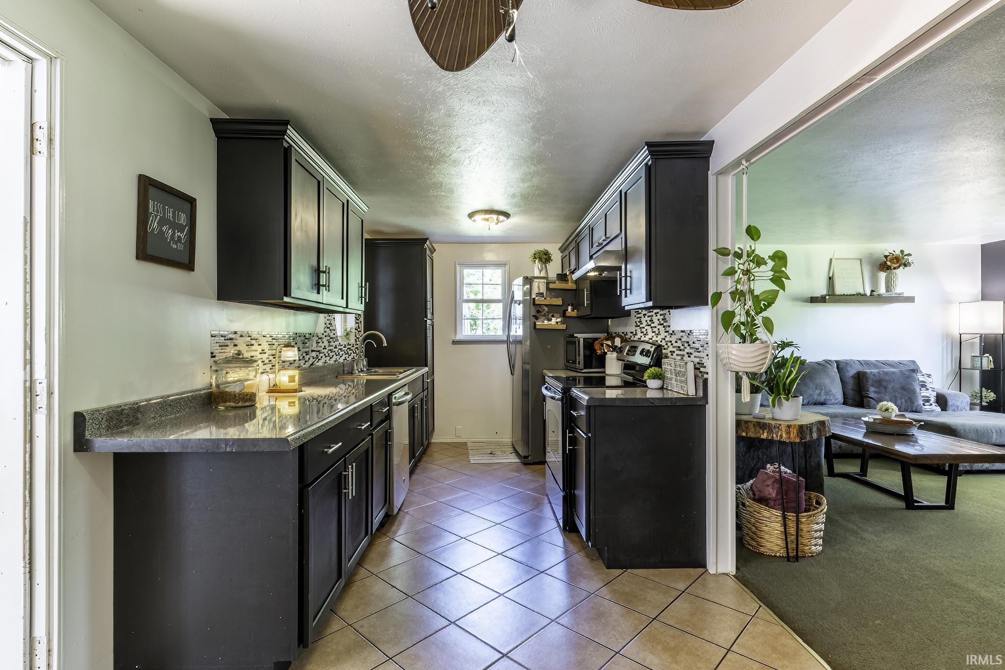 Galley kitchen featuring dark cabinetry, stainless steel appliances, a mosaic tile backsplash, and light-colored tile flooring