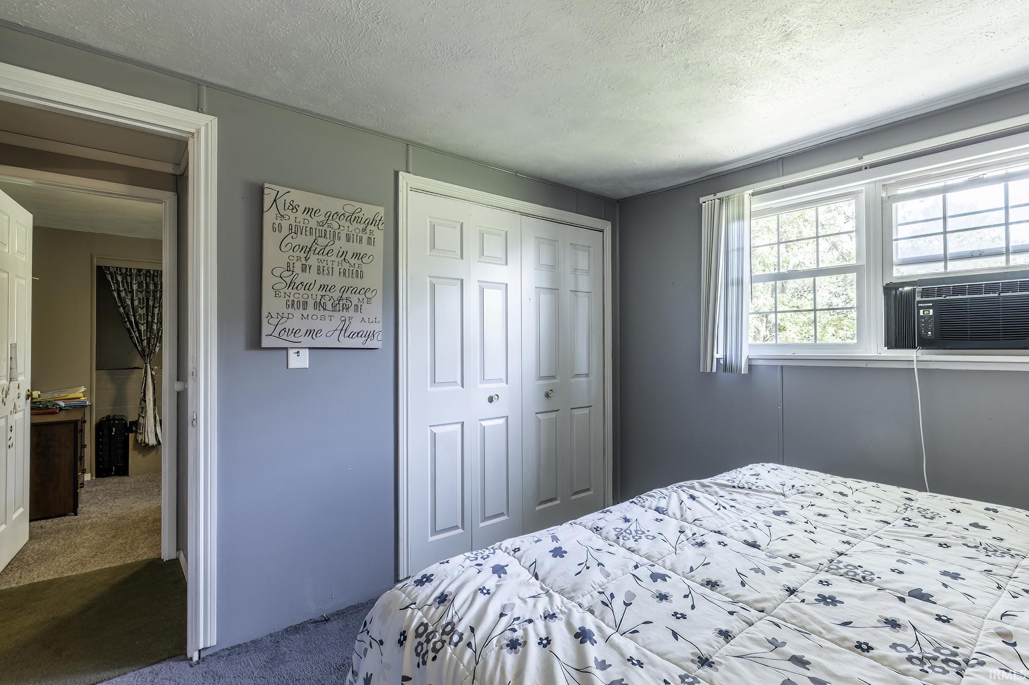 Bedroom featuring light gray wall paneling, a double window with white blinds, and gray carpeted flooring