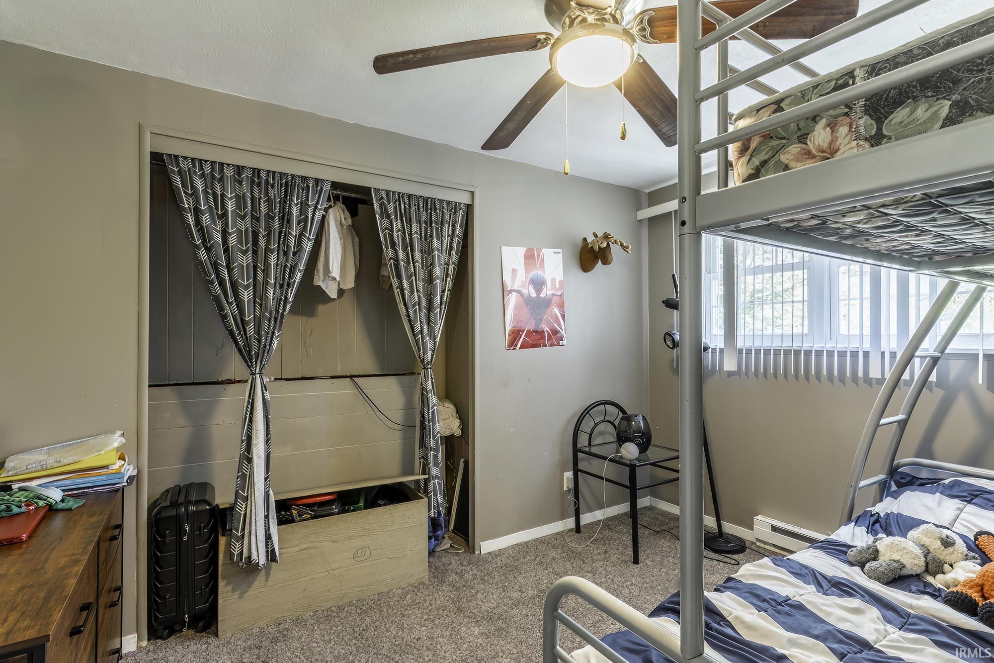 Carpeted room featuring a ceiling fan with integrated lighting, a window with vertical blinds, and a built-in closet area with curtain enclosures
