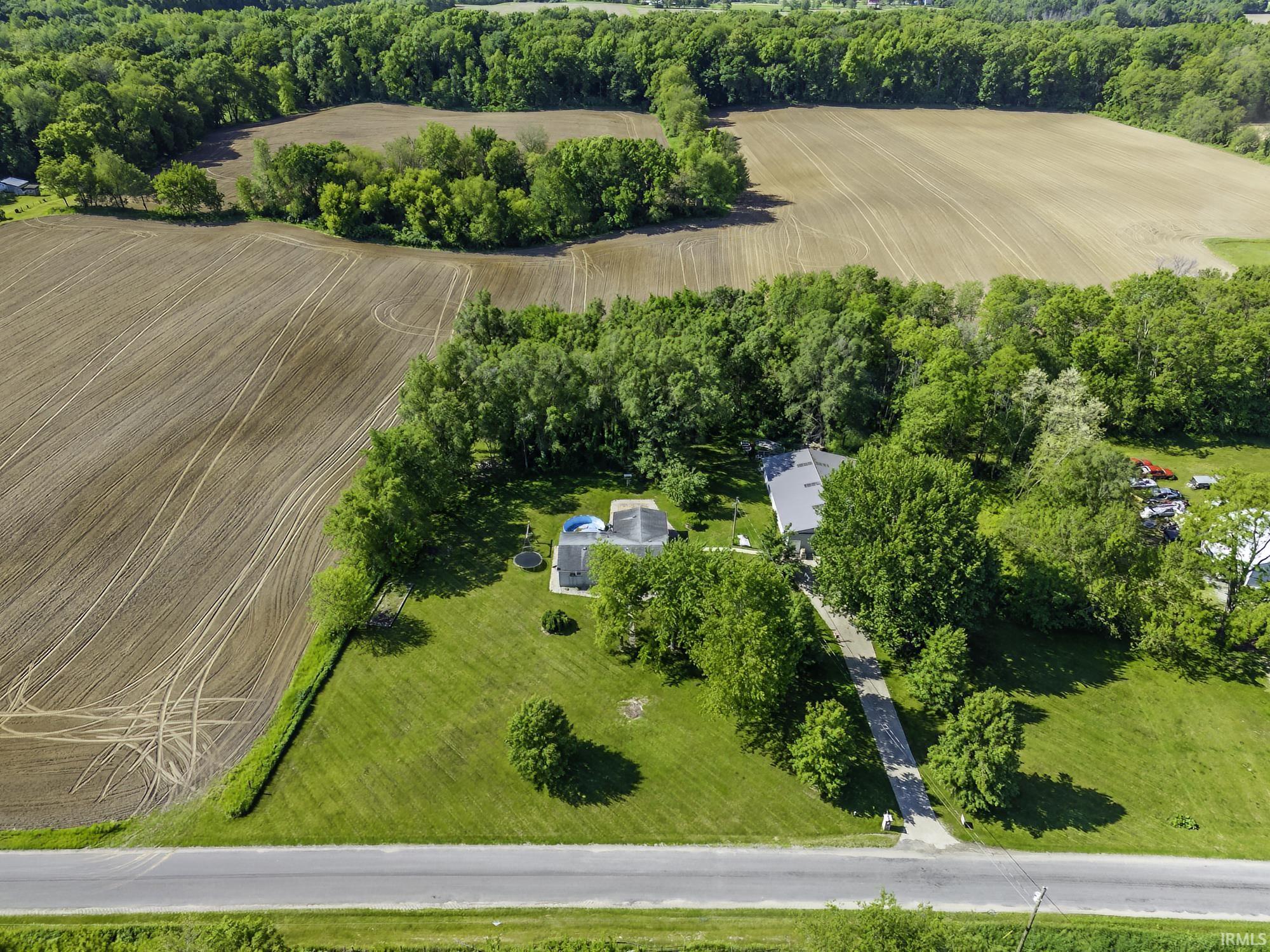 Aerial view showcasing a residential property with surrounding agricultural land and wooded areas