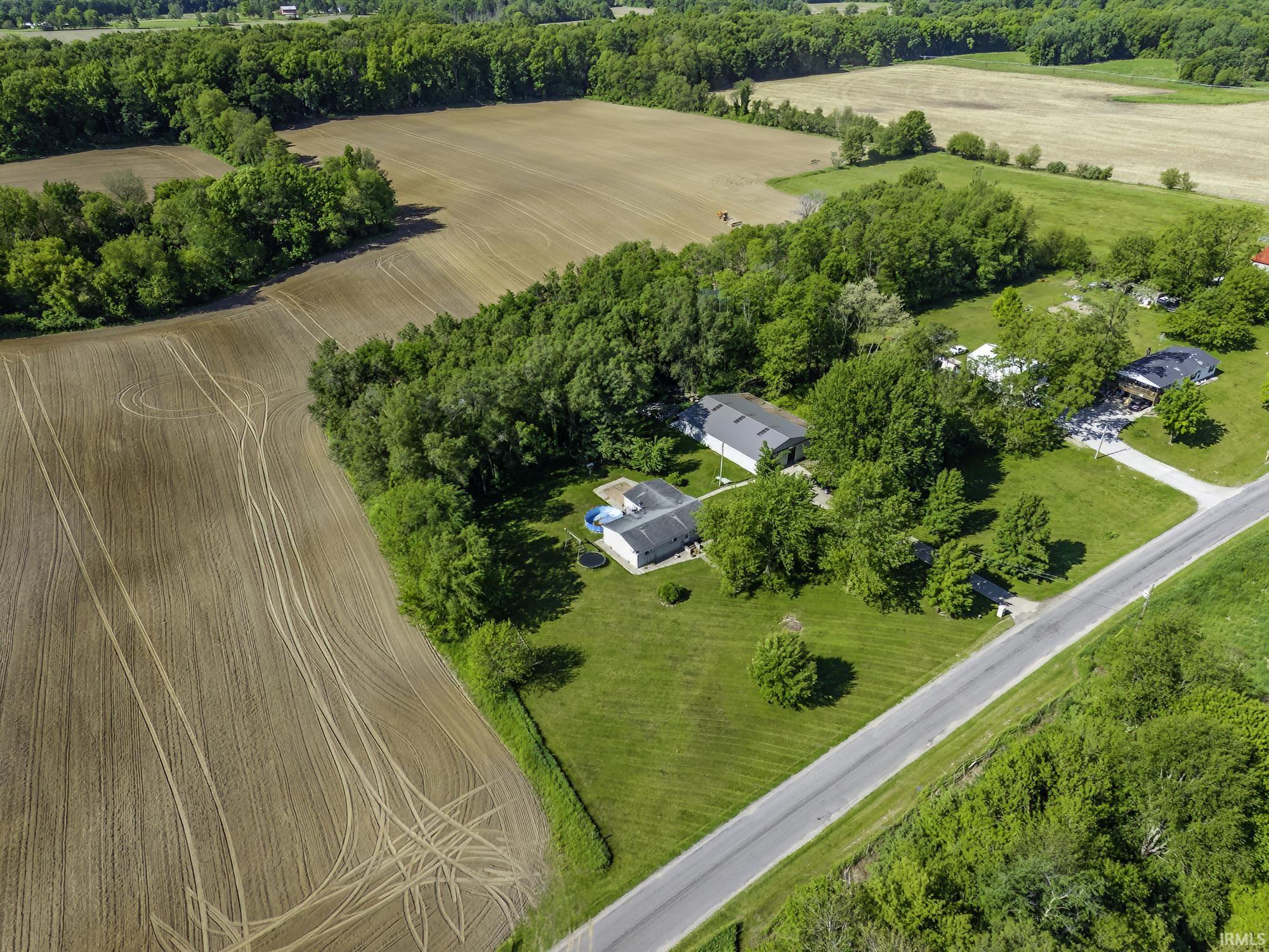 Expansive property featuring multiple structures, mature trees, a private road, and surrounding cultivated fields