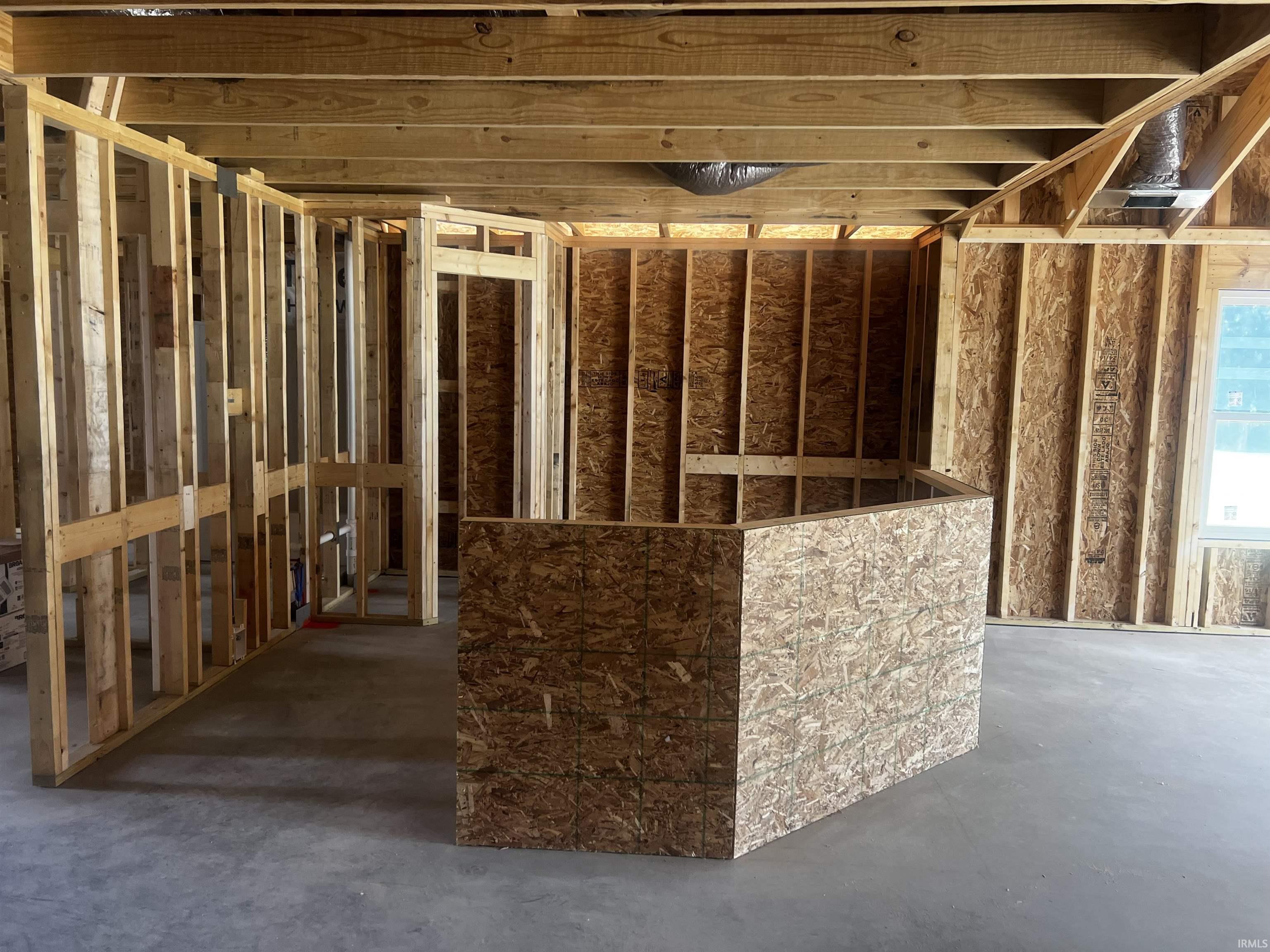 Unfinished interior framing with wood studs, engineered wood sheathing, exposed ceiling joists, and concrete flooring