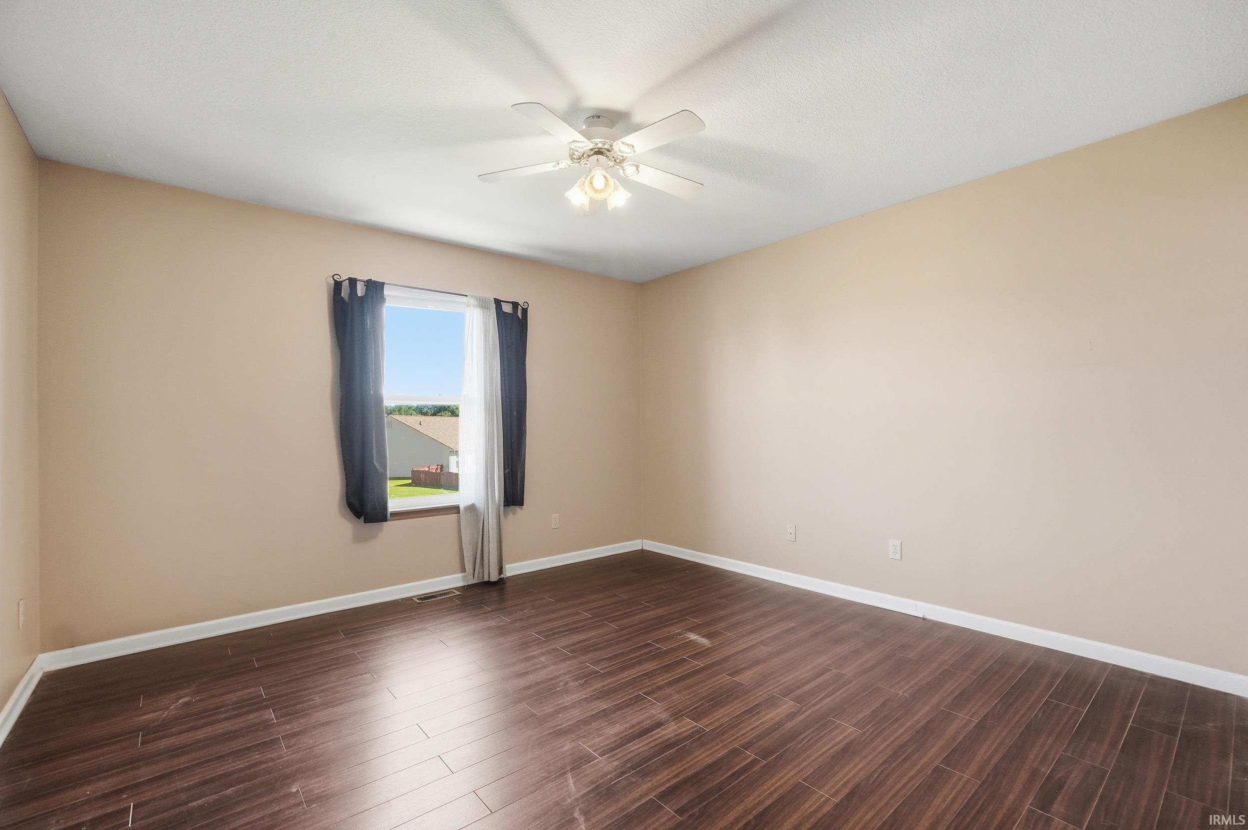 Spacious room featuring wood-finish flooring, neutral-toned walls, and a window with a neighborhood backdrop