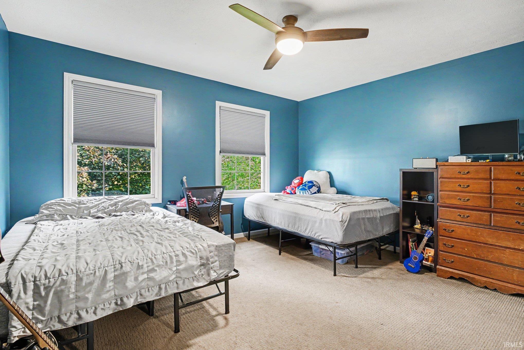 Room featuring two windows with privacy blinds, a ceiling fan with light fixture, and neutral carpet flooring