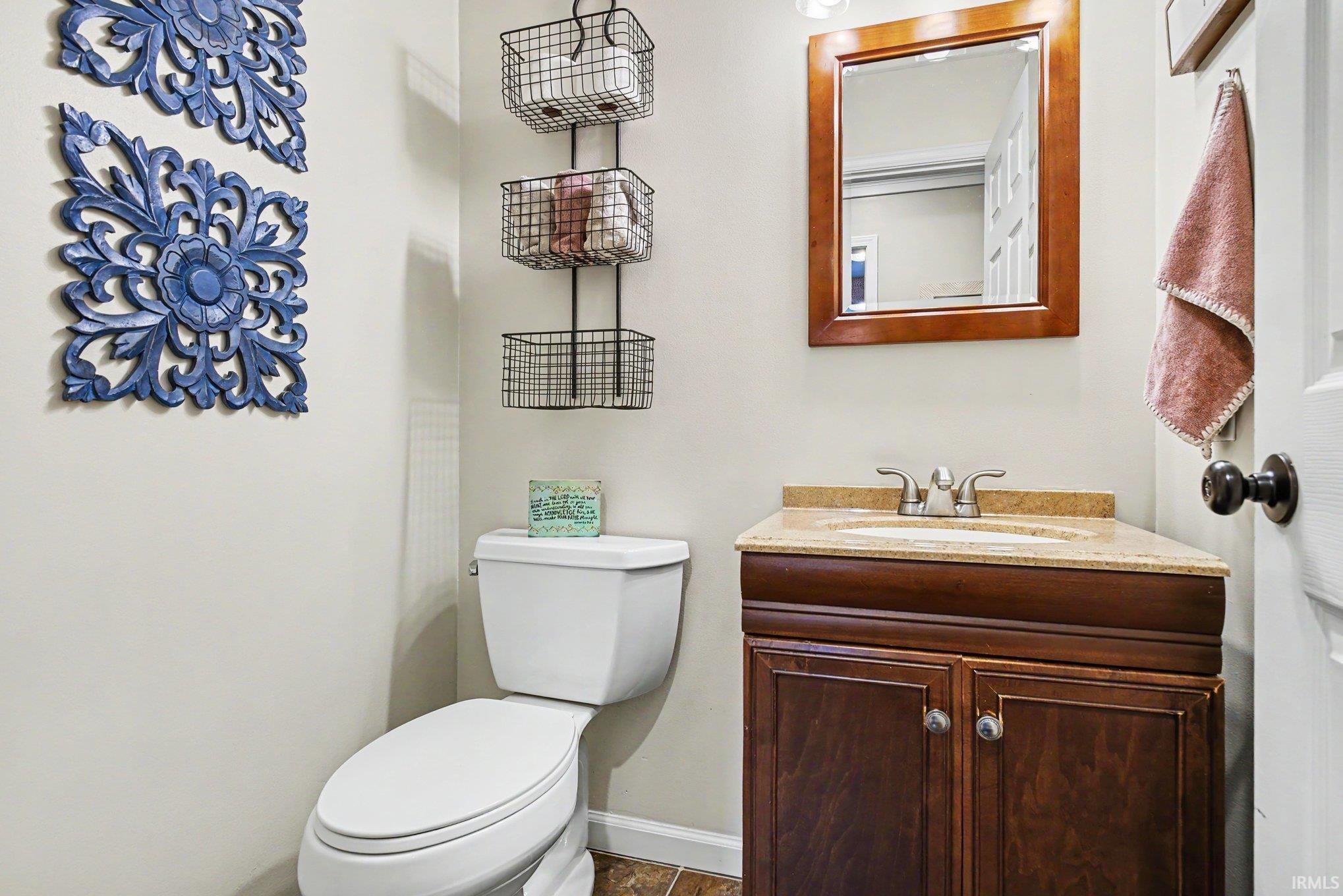 Powder room featuring a wood-finish vanity with a stone countertop, an undermount sink, and a framed mirror