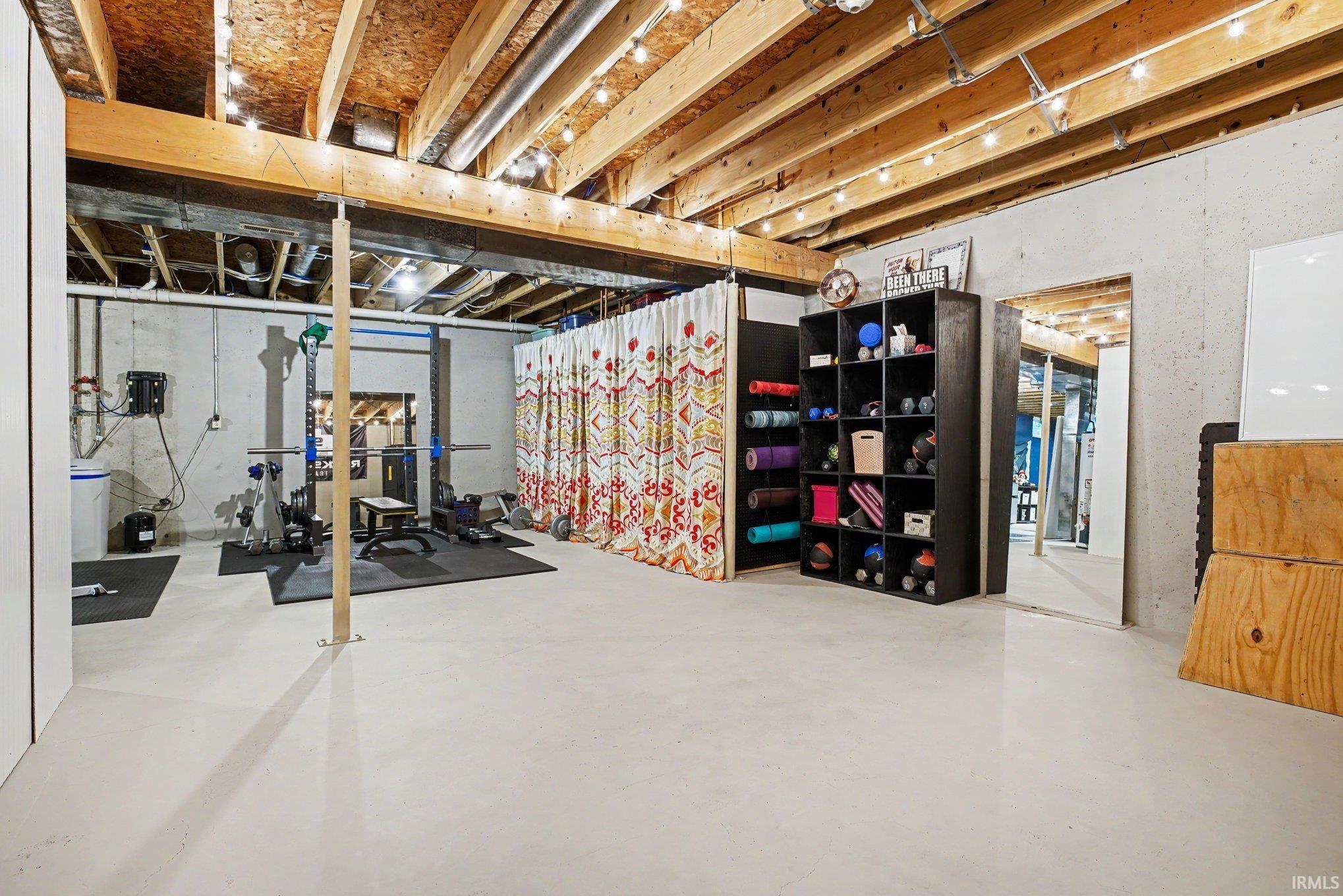 Exposed wood ceiling beams with string lighting, painted concrete flooring, and bare concrete walls