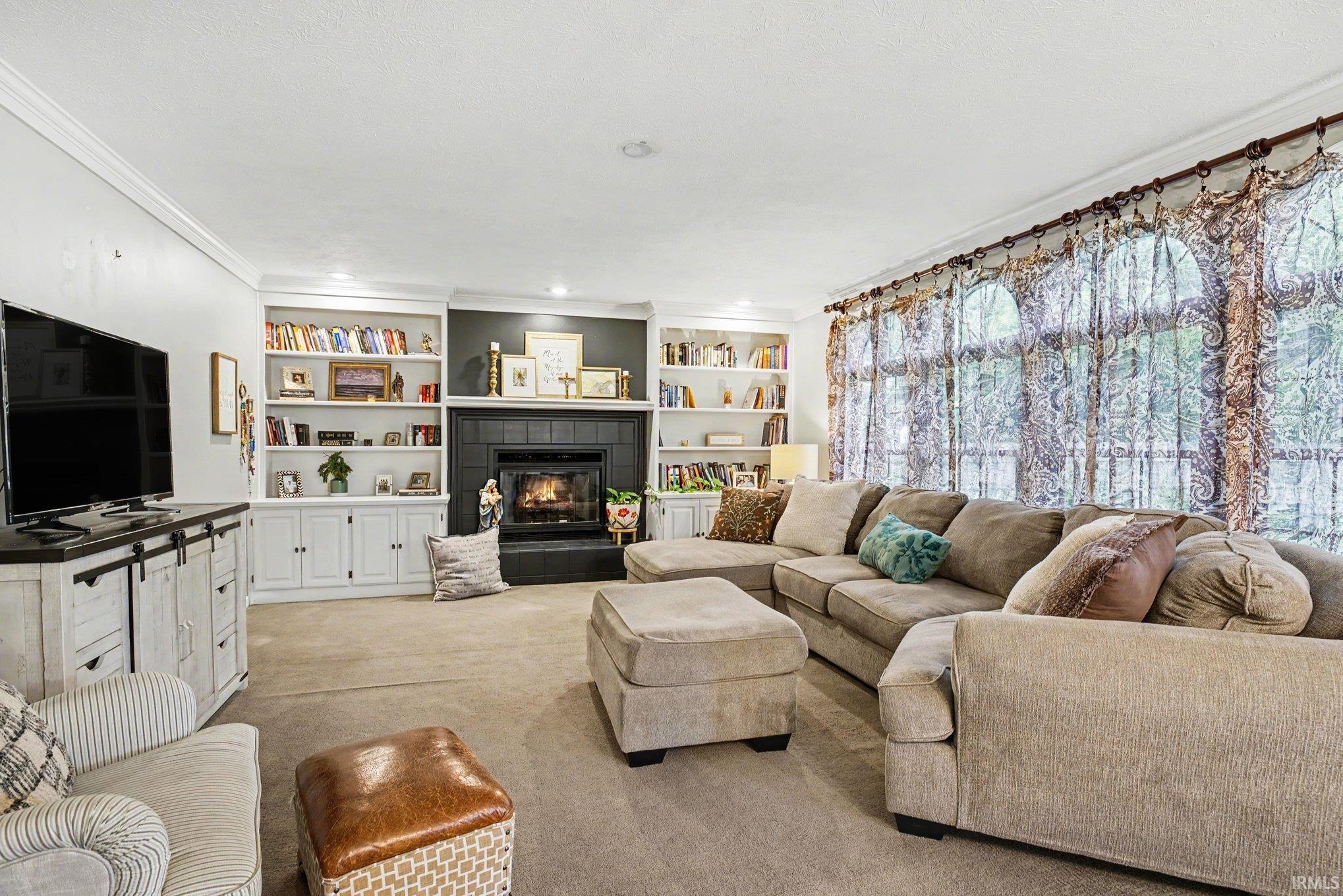 Living room featuring a fireplace with a dark tile surround, built-in shelving, crown molding, and large windows