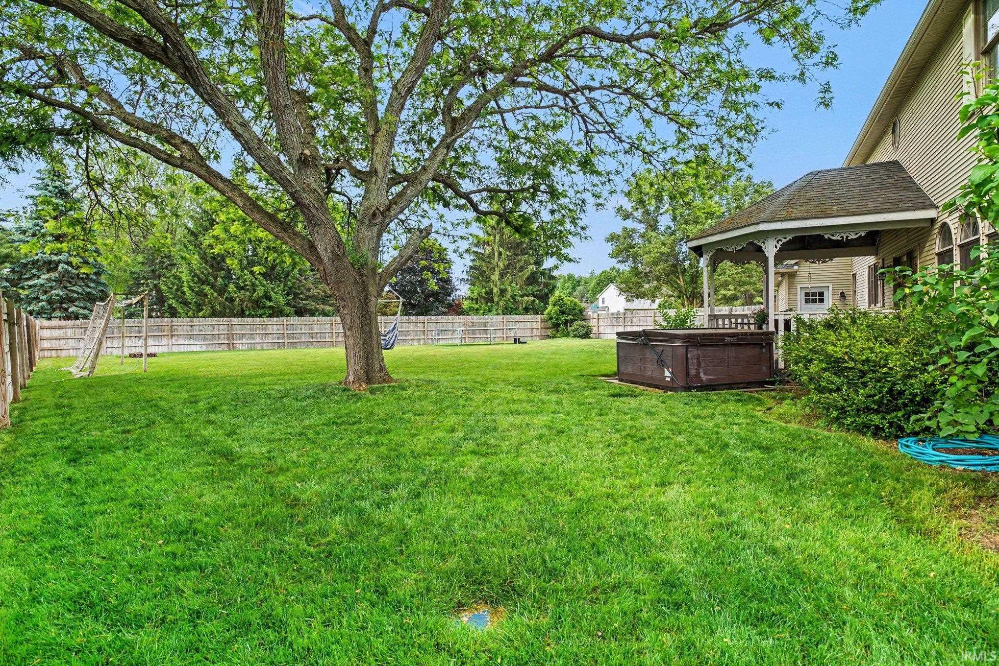 Expansive fenced backyard featuring a mature shade tree, a built-in hot tub, and a decorative gazebo with a railing