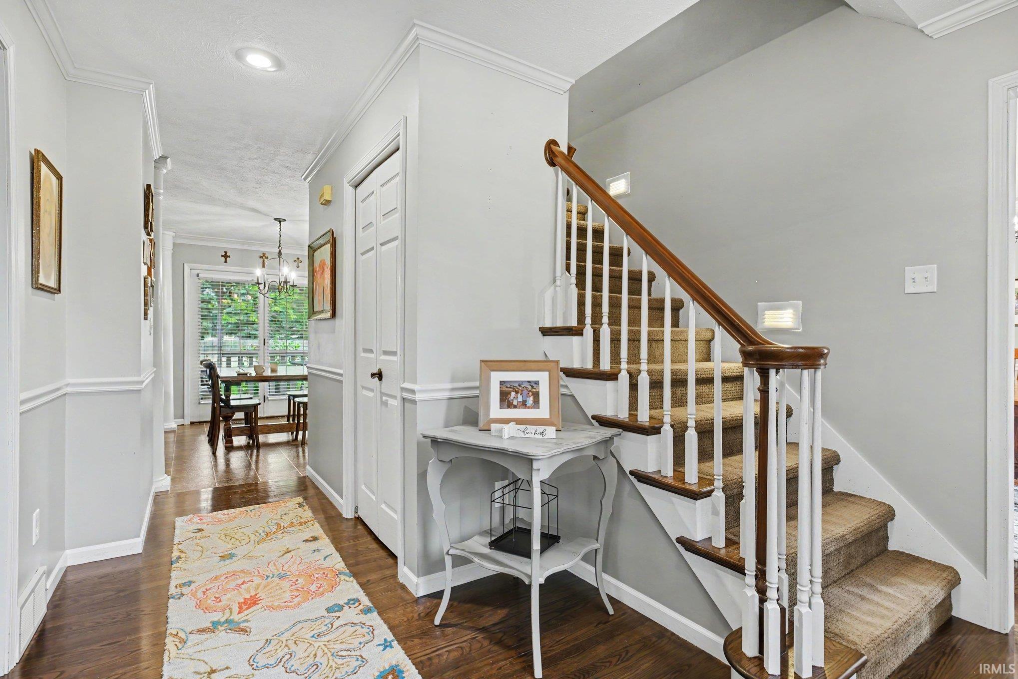Entryway featuring wood-finish flooring, a carpeted staircase with wood handrails and white balusters, and a recessed ceiling light