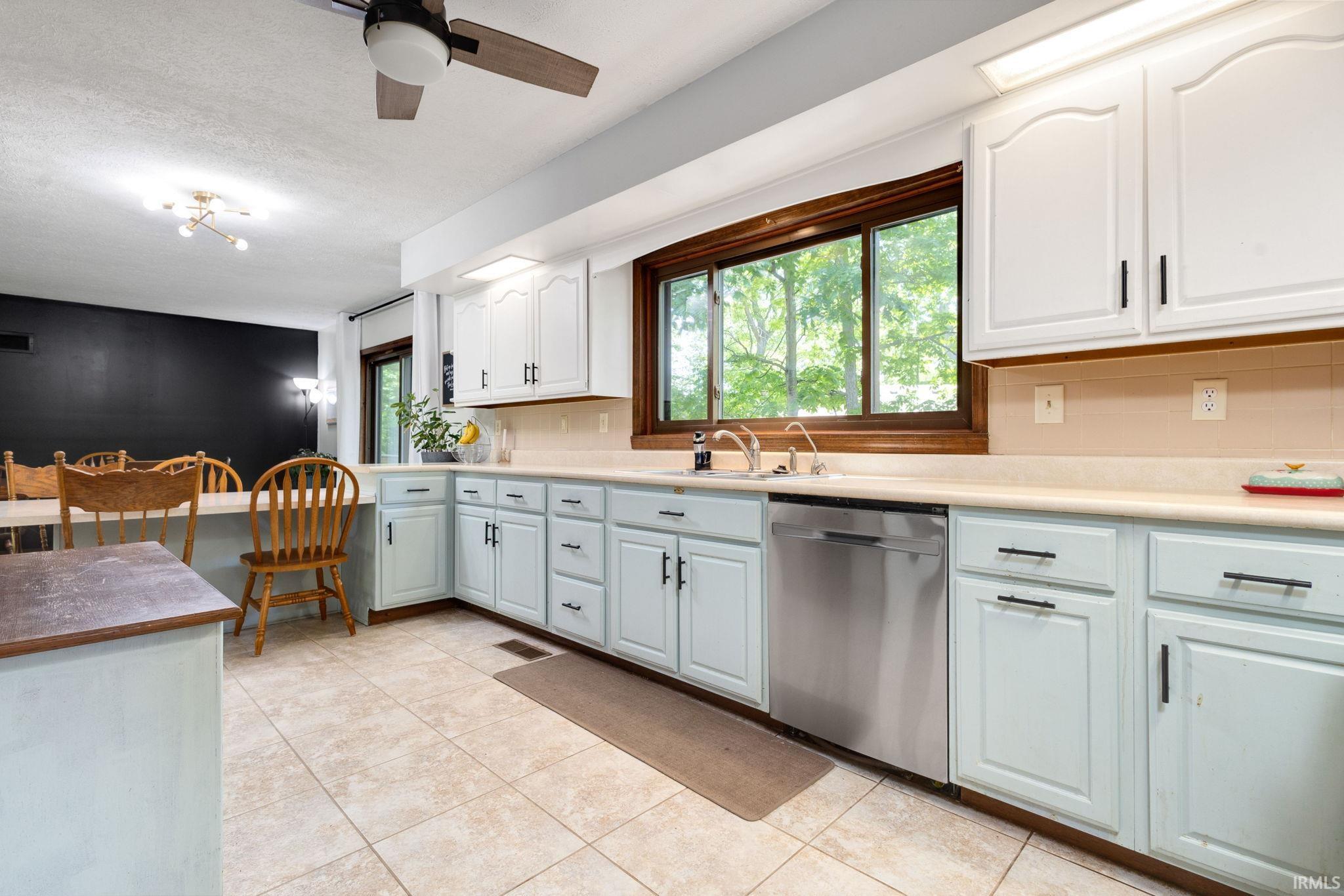 Bright kitchen featuring a stainless steel dishwasher, light-toned countertops, and a wood-framed window