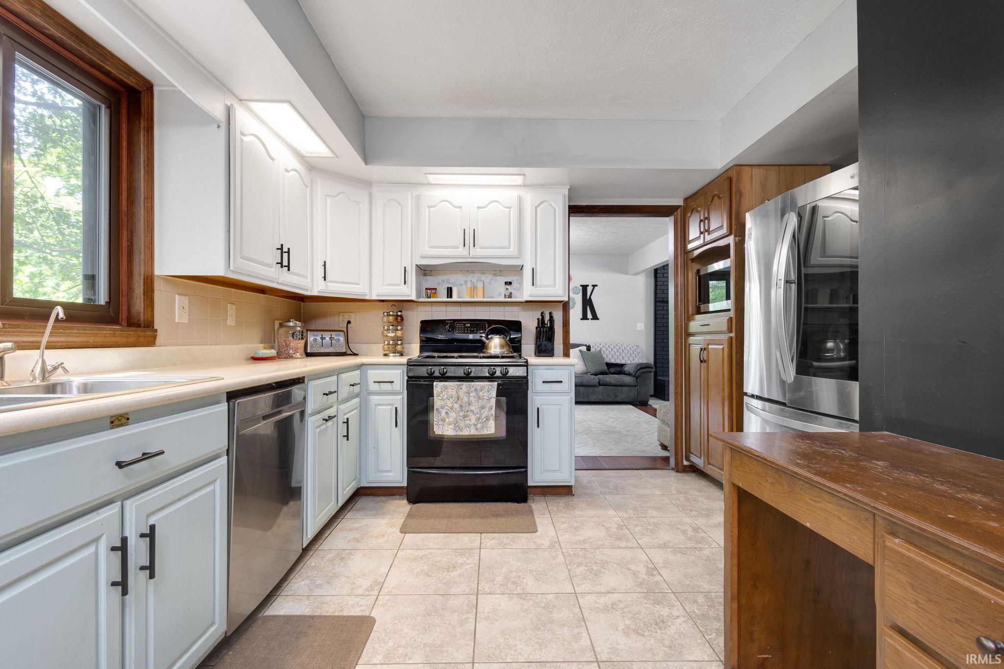 Kitchen featuring two-tone cabinetry with black hardware, stainless steel appliances, a built-in oven, and wood-finish trim around a large window