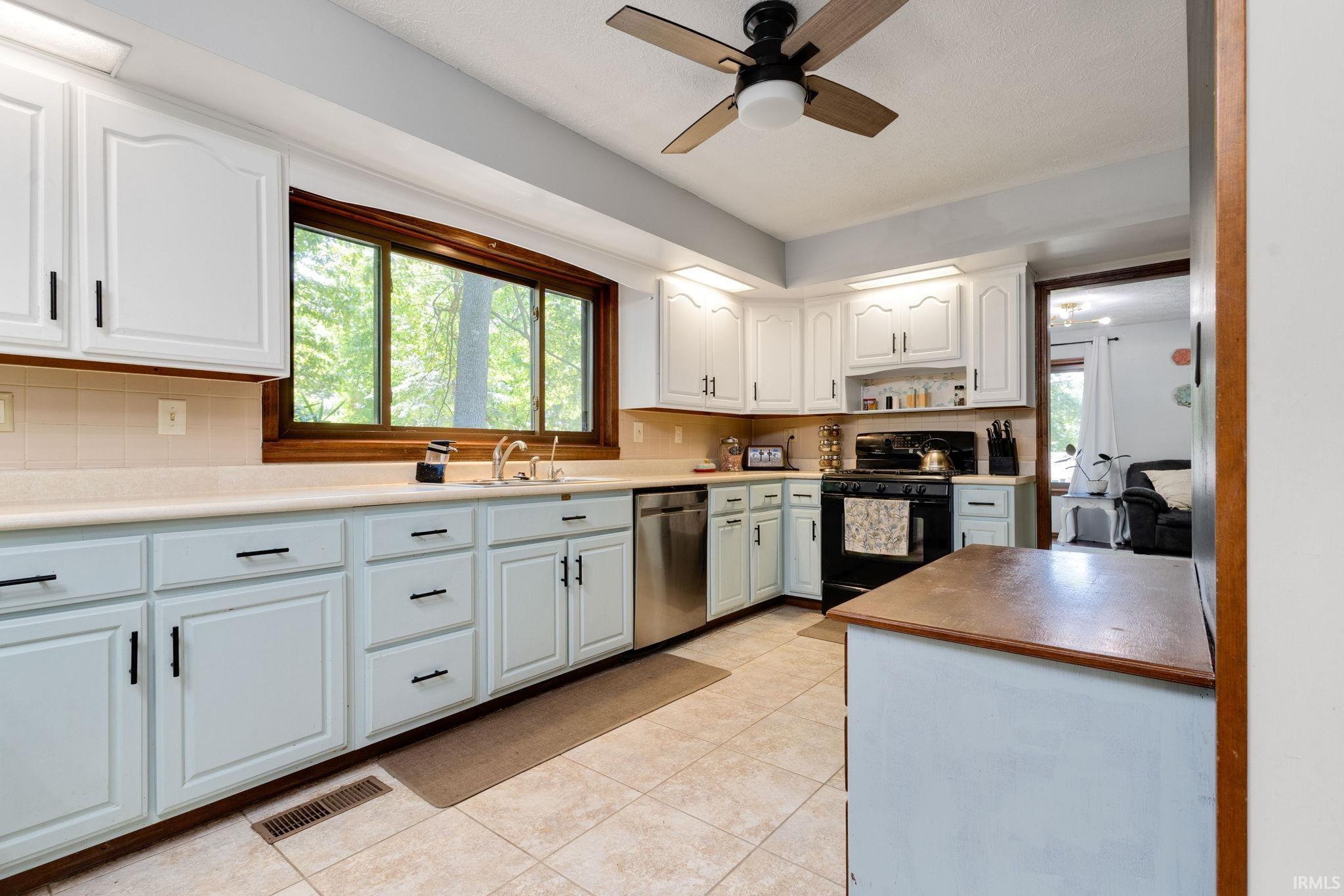 Kitchen featuring a large window, light-toned tiled flooring, white upper cabinetry, and light blue lower cabinetry with dark hardware