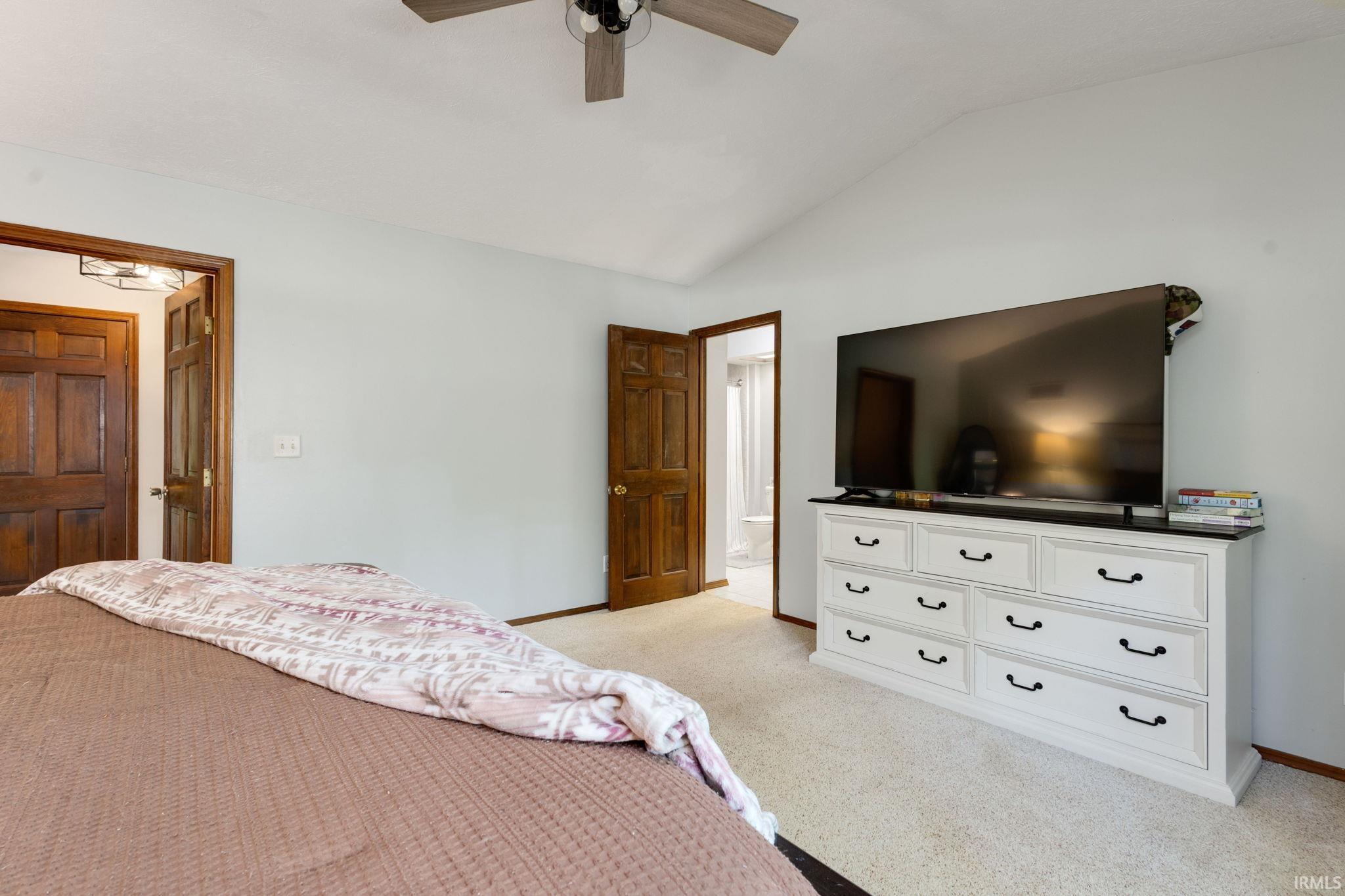 Bedroom featuring vaulted ceilings, light-toned carpeting, and warm wood-paneled doors