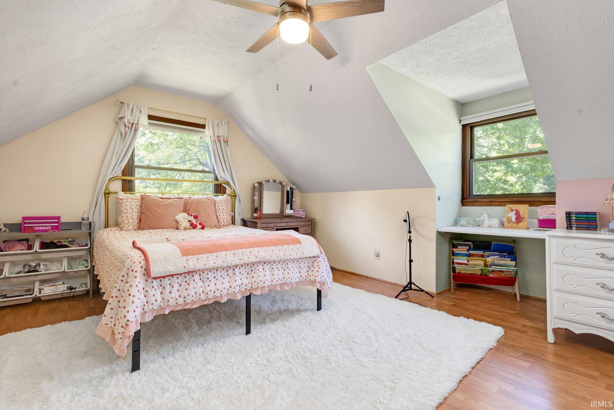 Attic room featuring sloped ceilings, wood-finish flooring, and a ceiling fan with integrated lighting
