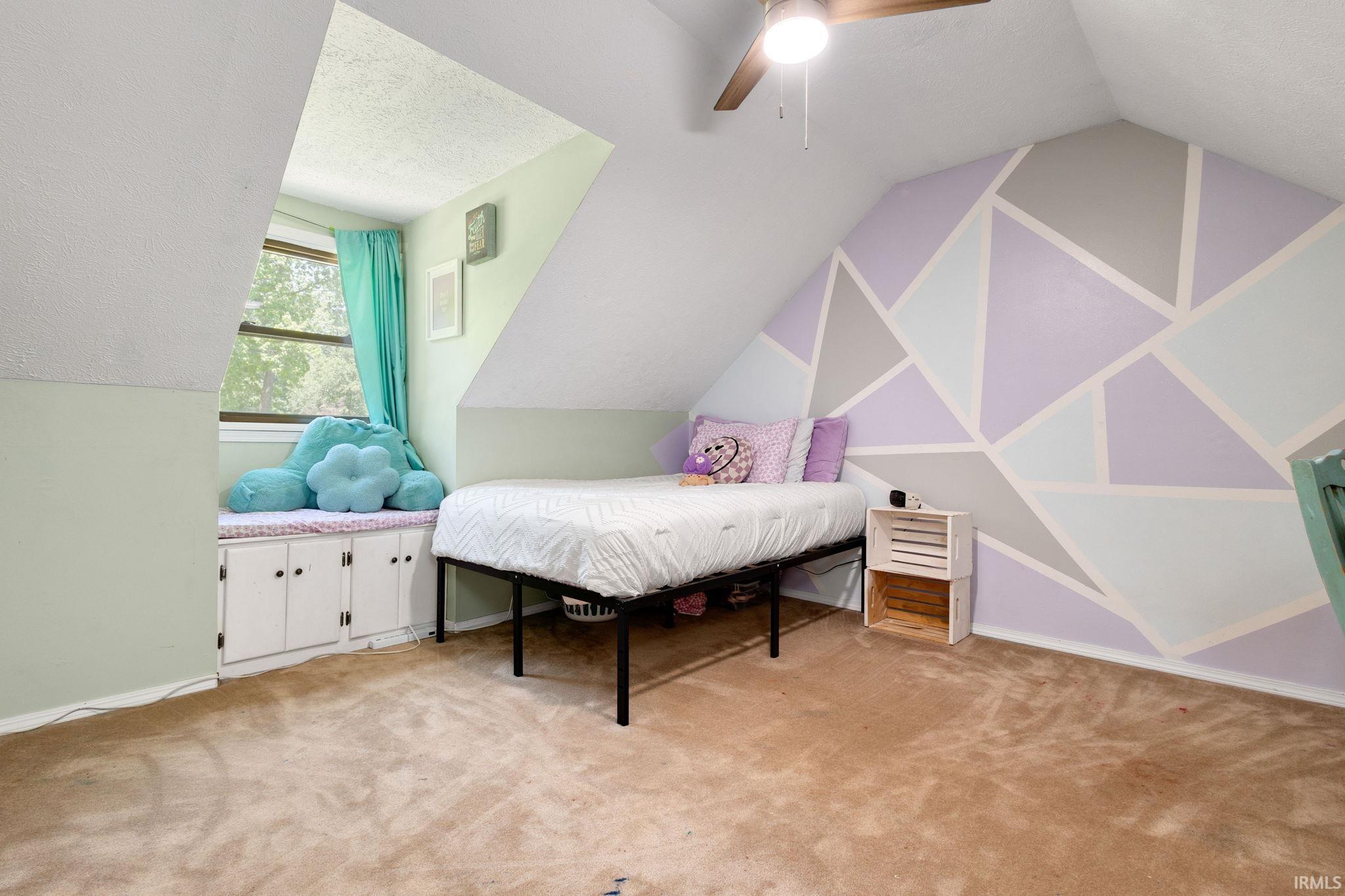 Room featuring sloped ceilings, a geometric accent wall, and a built-in window seat with cabinetry