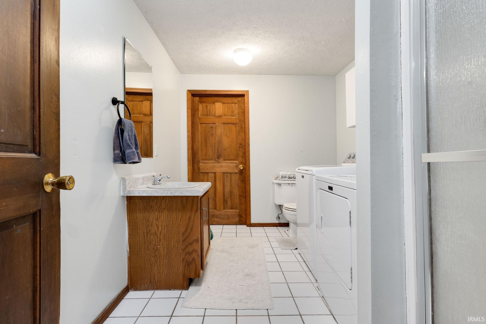 Utility room featuring a built-in sink vanity with a laminate countertop, washer and dryer units, and white square floor tiling