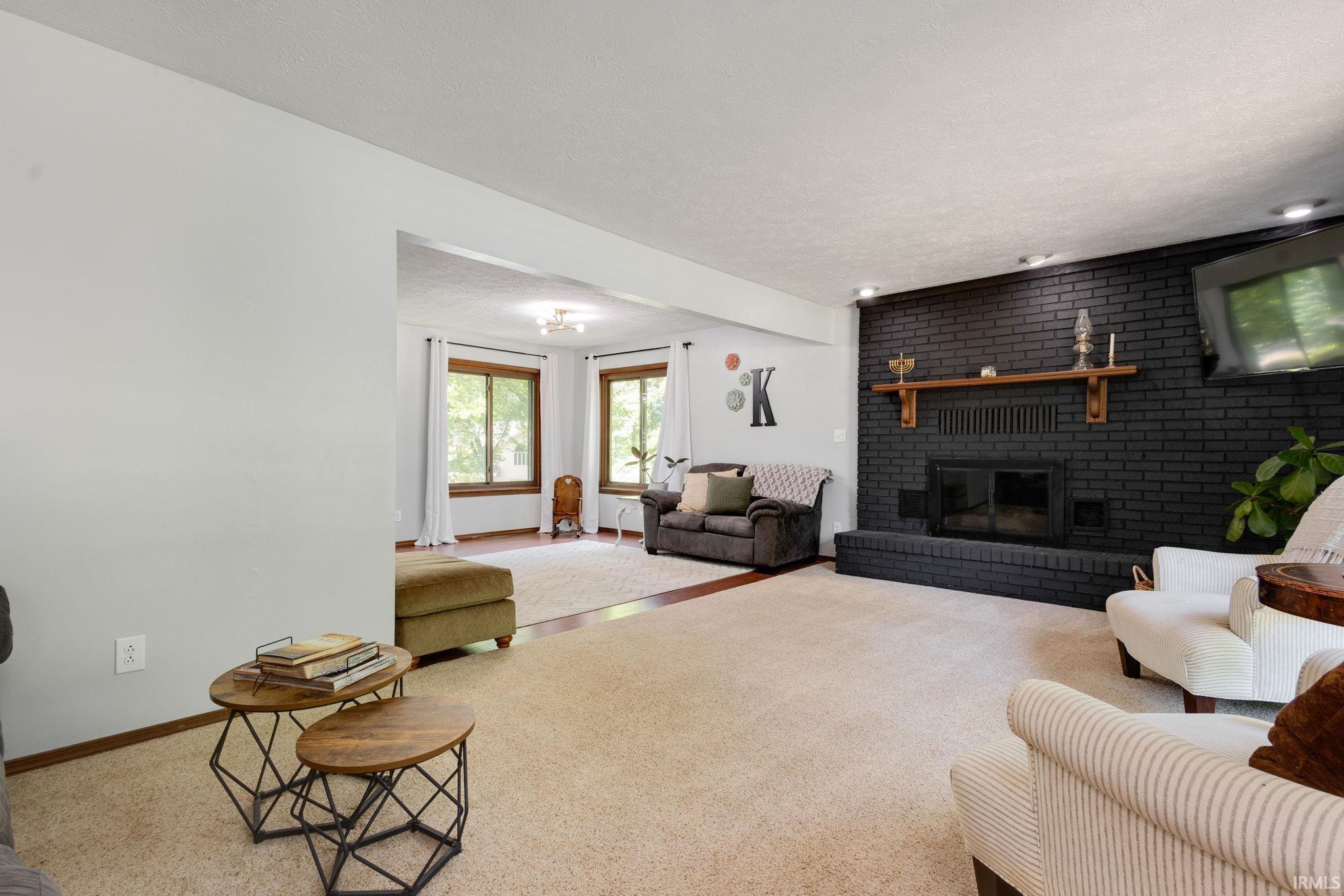 Spacious living area featuring a black painted brick fireplace with a wood mantel