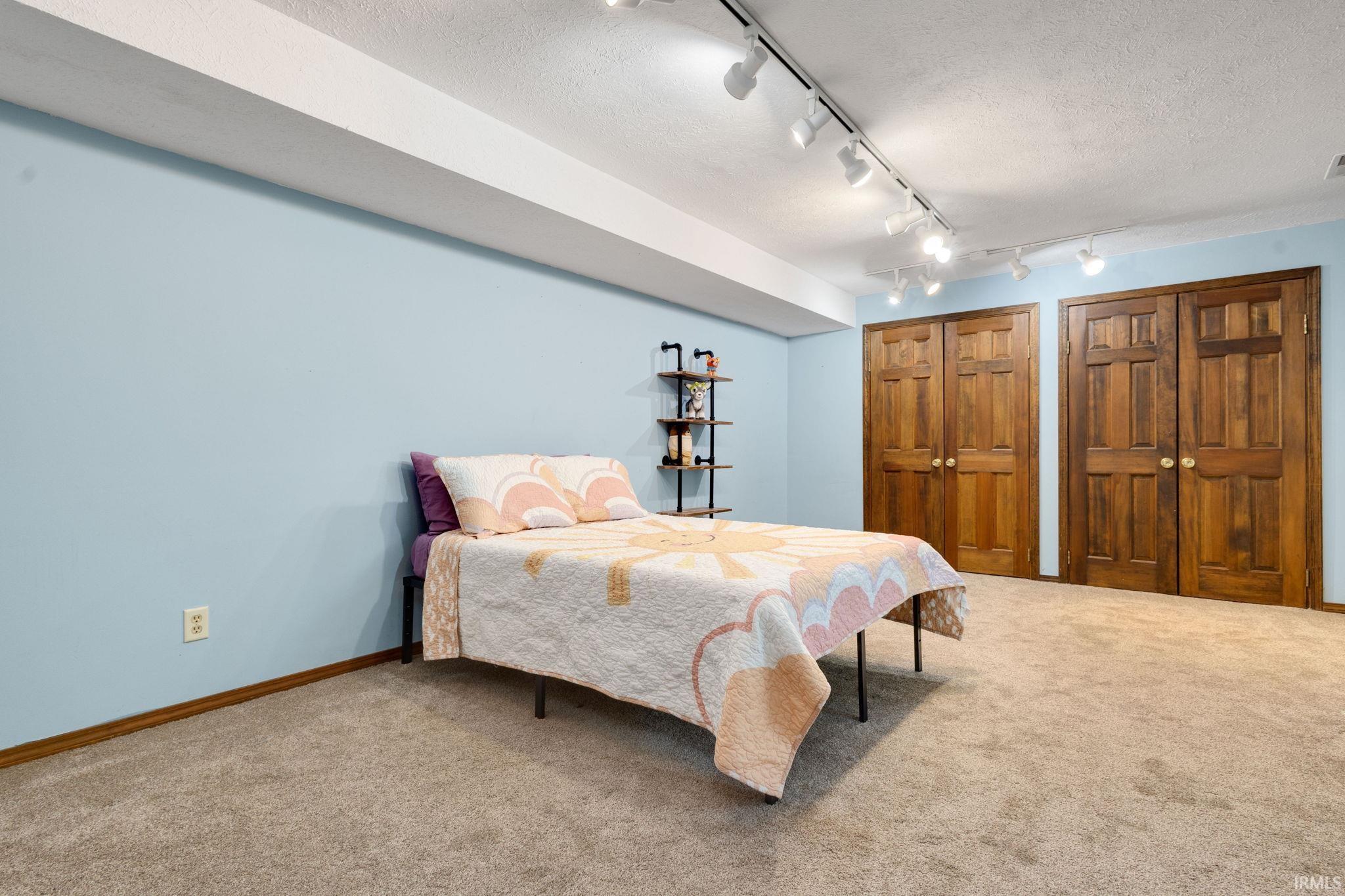 Spacious room featuring light blue walls, two sets of paneled wood-finish double doors, and track lighting
