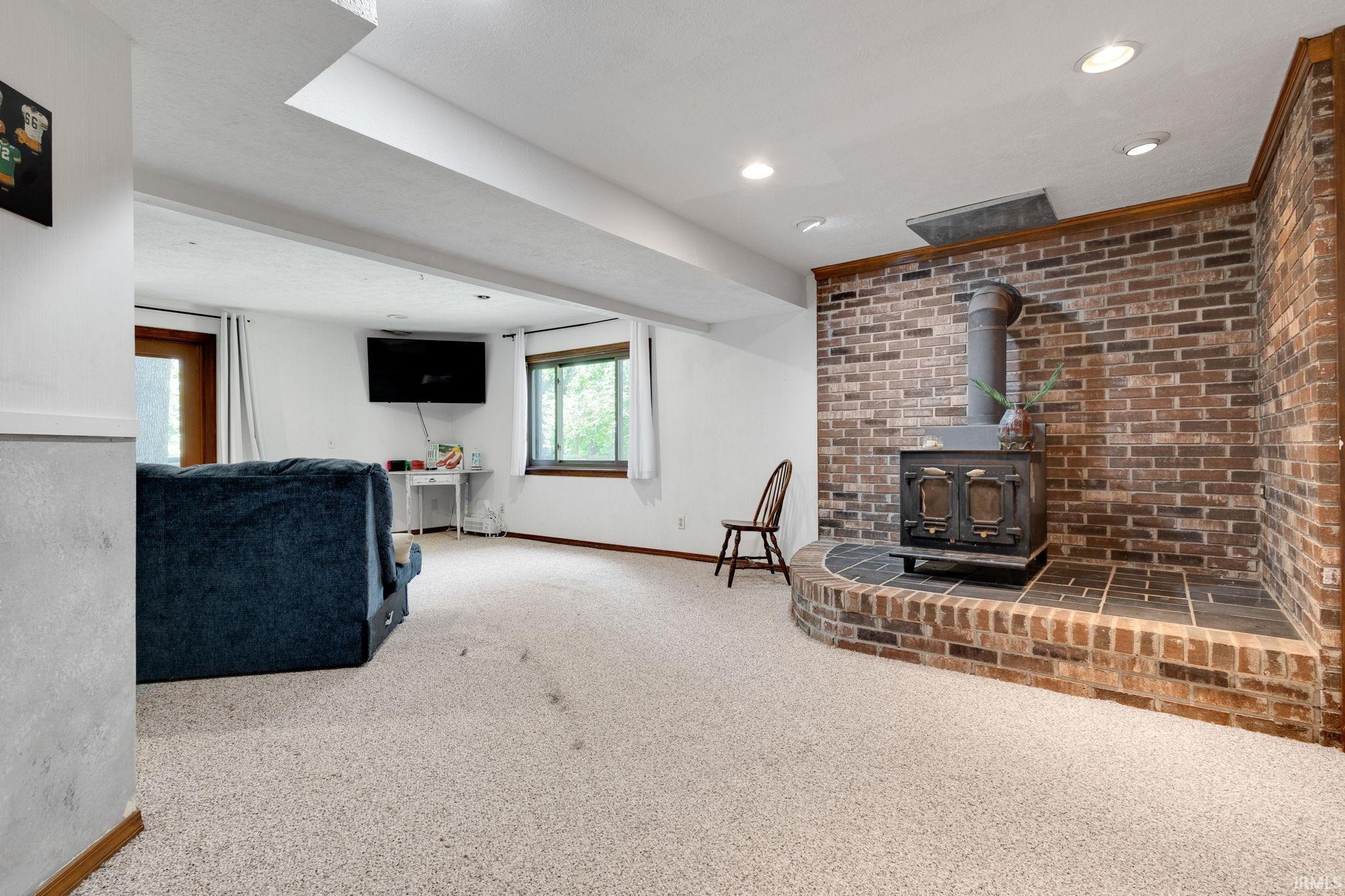 Expansive carpeted room featuring a prominent brick accent wall with a built-in wood-burning stove and hearth