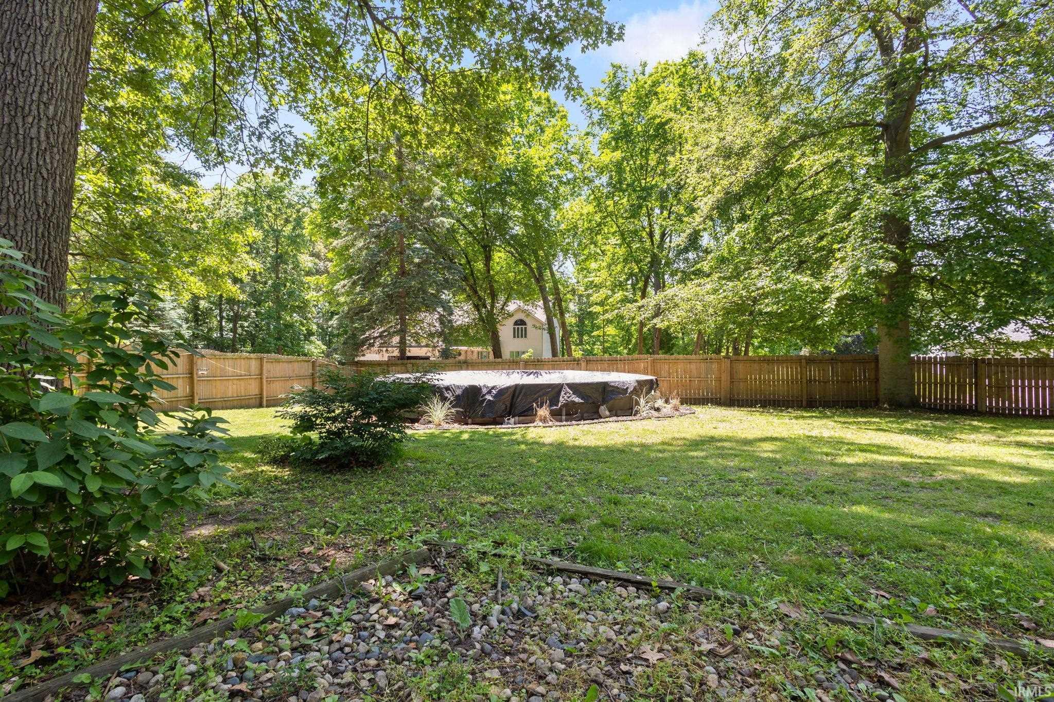 Expansive backyard featuring a covered above-ground pool, mature trees, manicured lawn, and wood privacy fencing