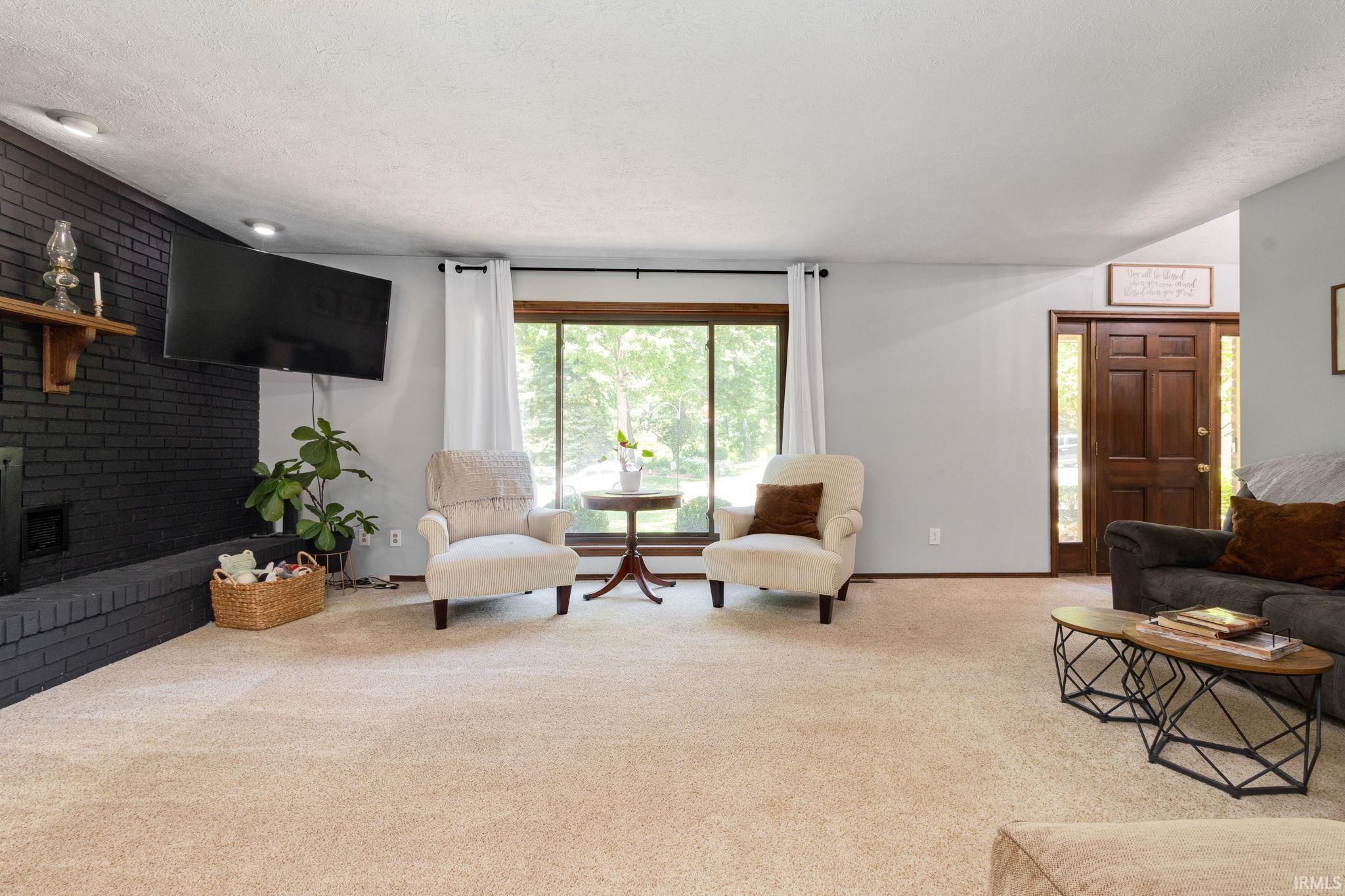 Spacious living area featuring a black brick fireplace, large picture window, and vaulted ceiling