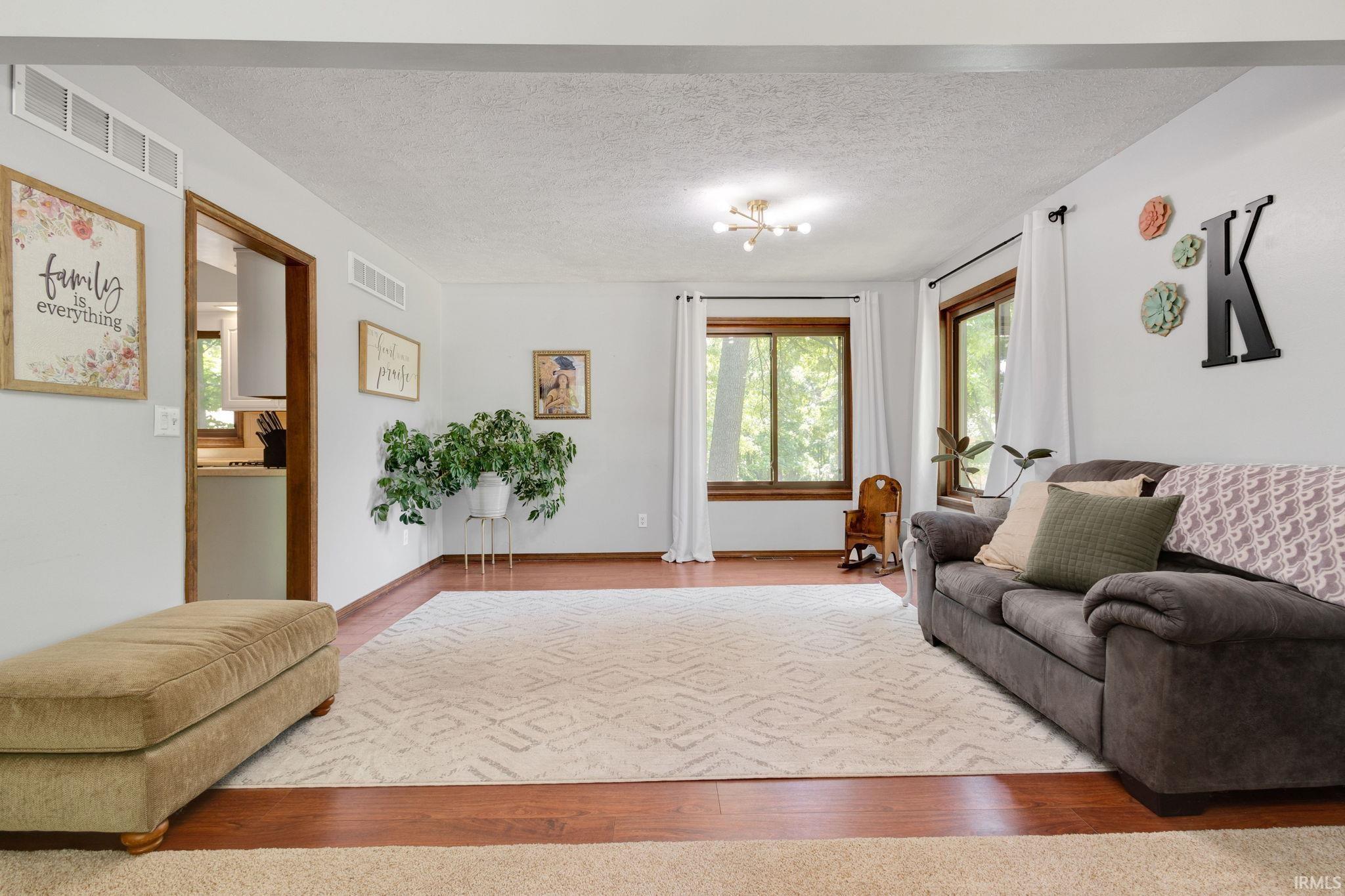 Spacious living area featuring wood-finish flooring, white walls, and multiple large windows with wood trim