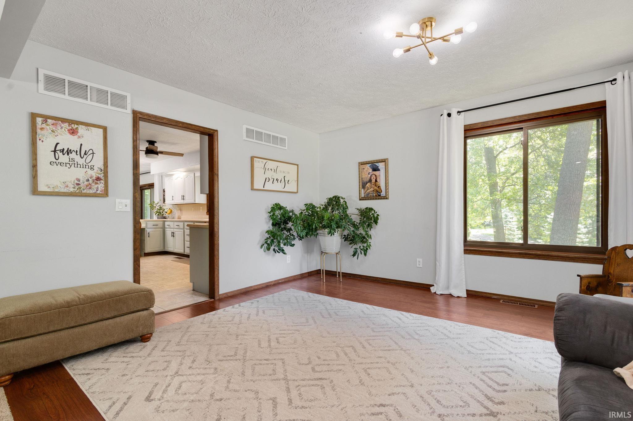 Living area featuring wood-finish flooring, a large window with wood trim, and a contemporary ceiling light fixture