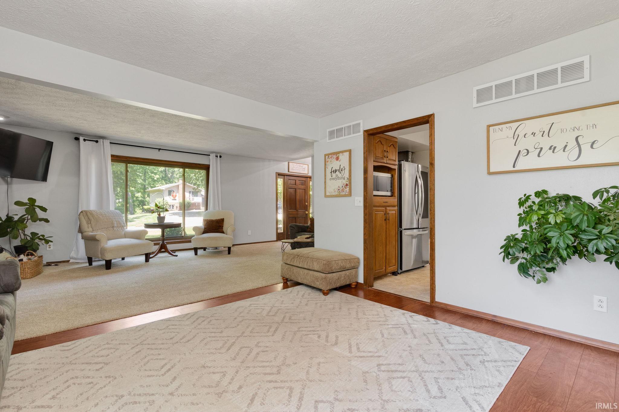 Open-concept living area featuring a large picture window, carpeted flooring, wood-finish flooring accents, and painted walls