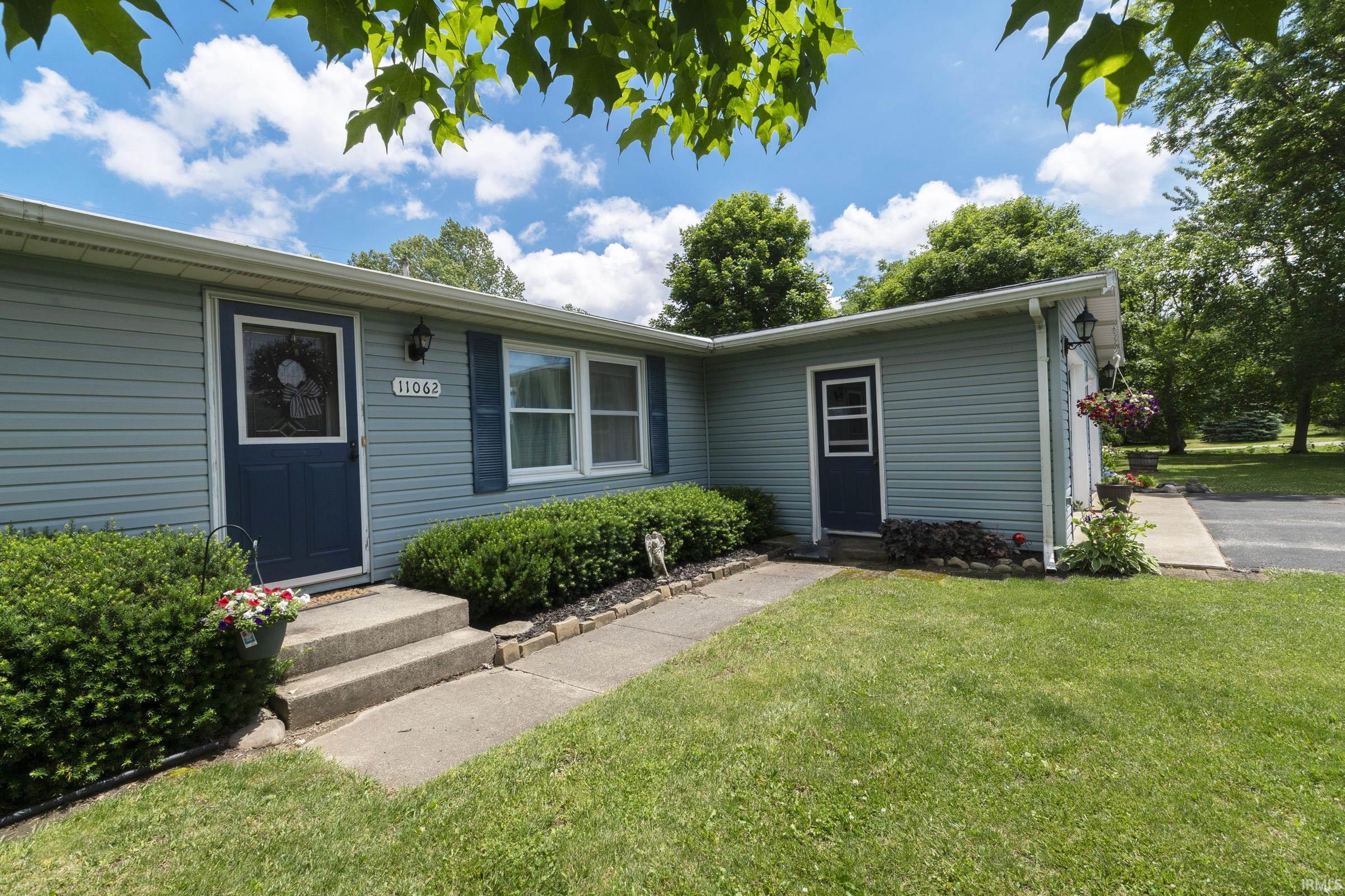 Light blue horizontal siding facade featuring a dark blue entry door with a storm door, white window frames, and dark blue shutters