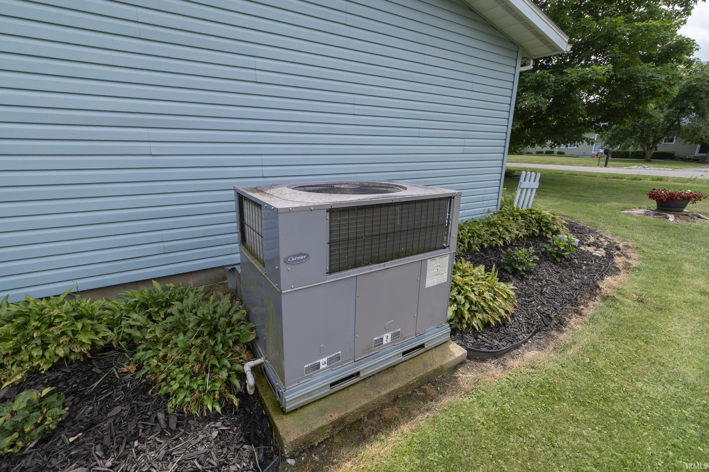 Exterior siding with an HVAC unit on a concrete pad, surrounded by mulched landscaping and partial lawn
