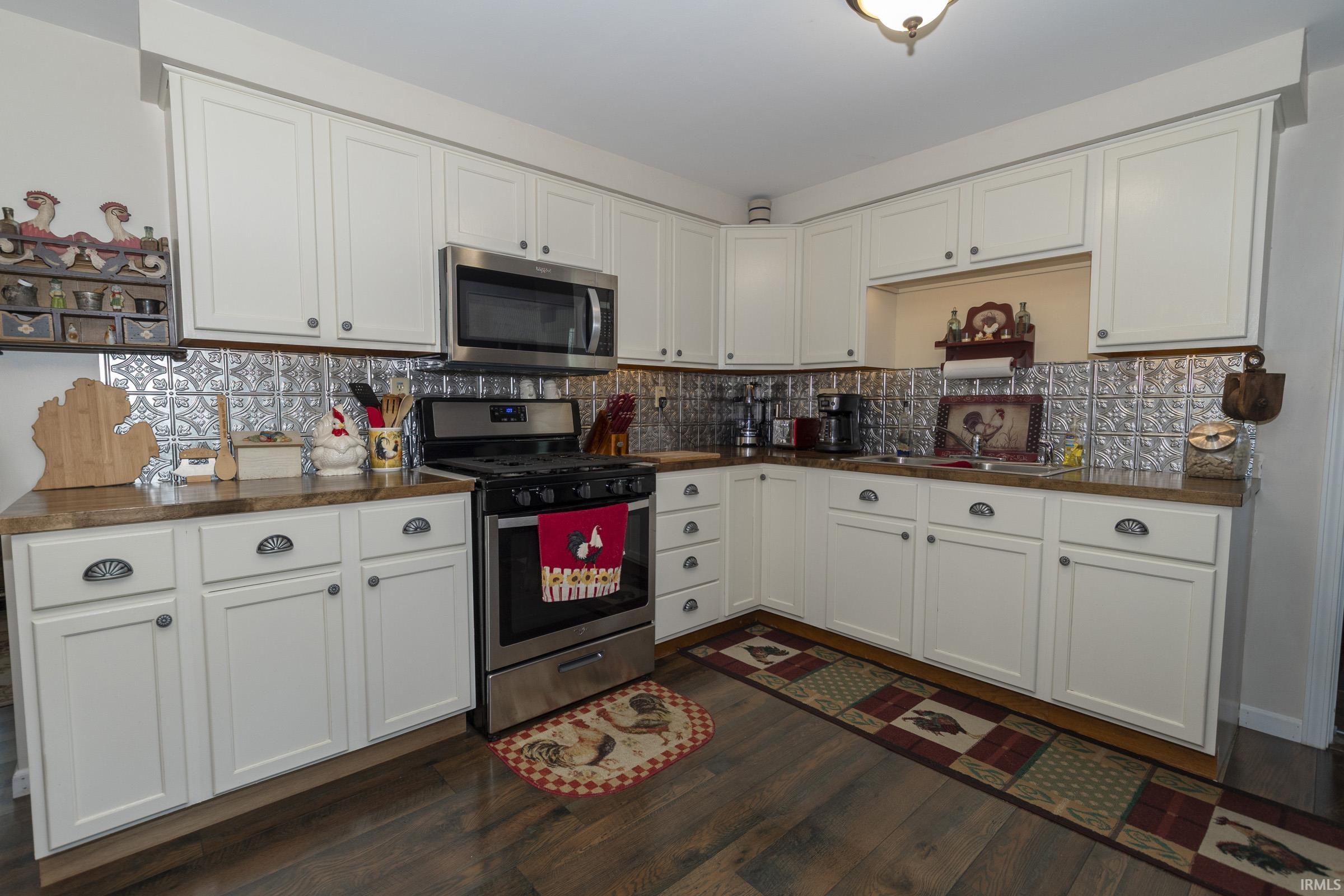 Kitchen featuring white cabinetry, stainless steel appliances, wood-finish flooring, a patterned tile backsplash, and dark countertops