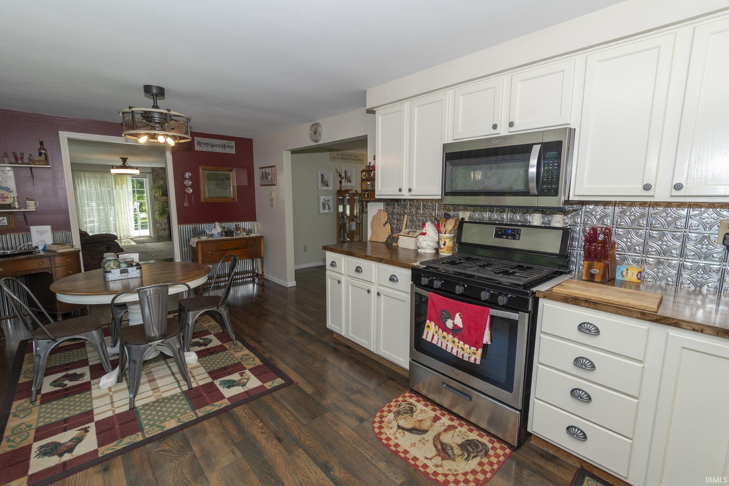 Kitchen featuring white cabinetry, stainless steel appliances, pressed tin backsplash, wood-finish flooring, and a dining area with a ceiling fan