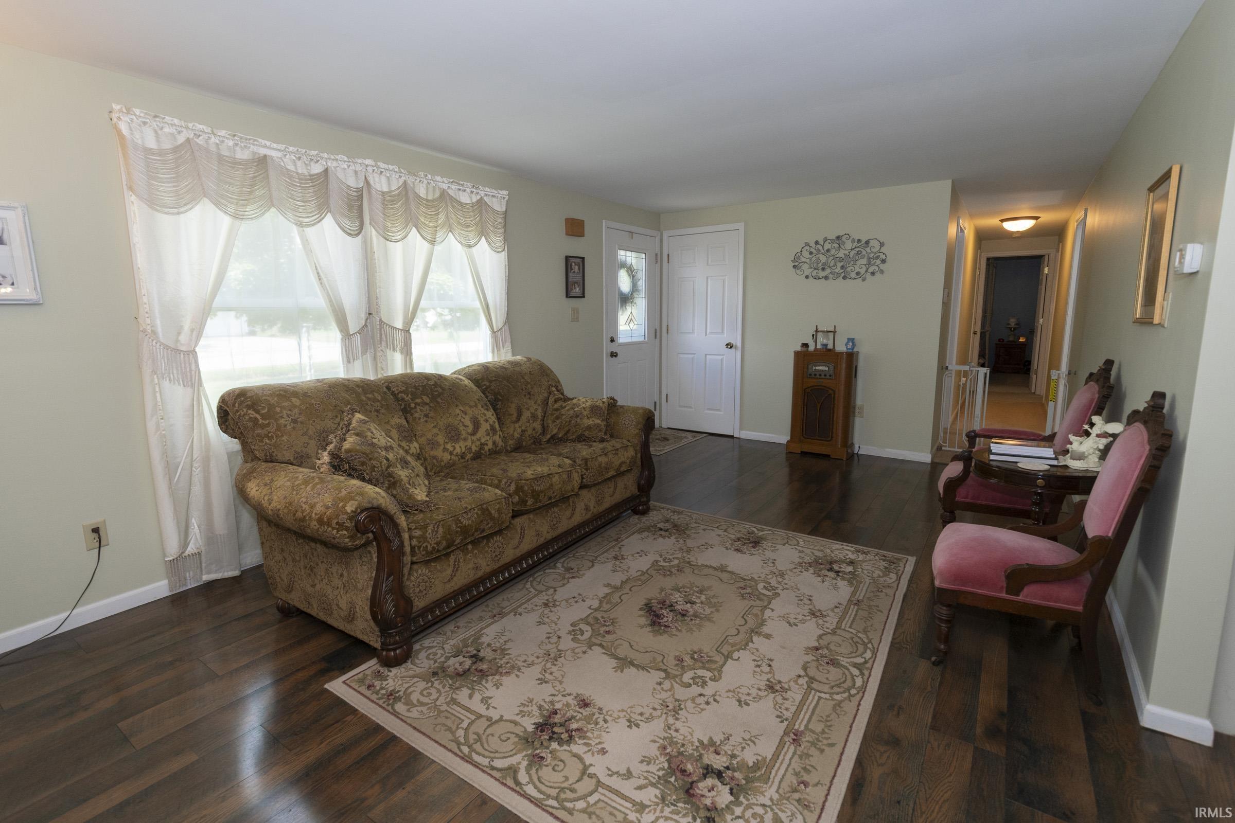 Living area featuring wood-finish flooring, light-toned walls, and a large window with sheers