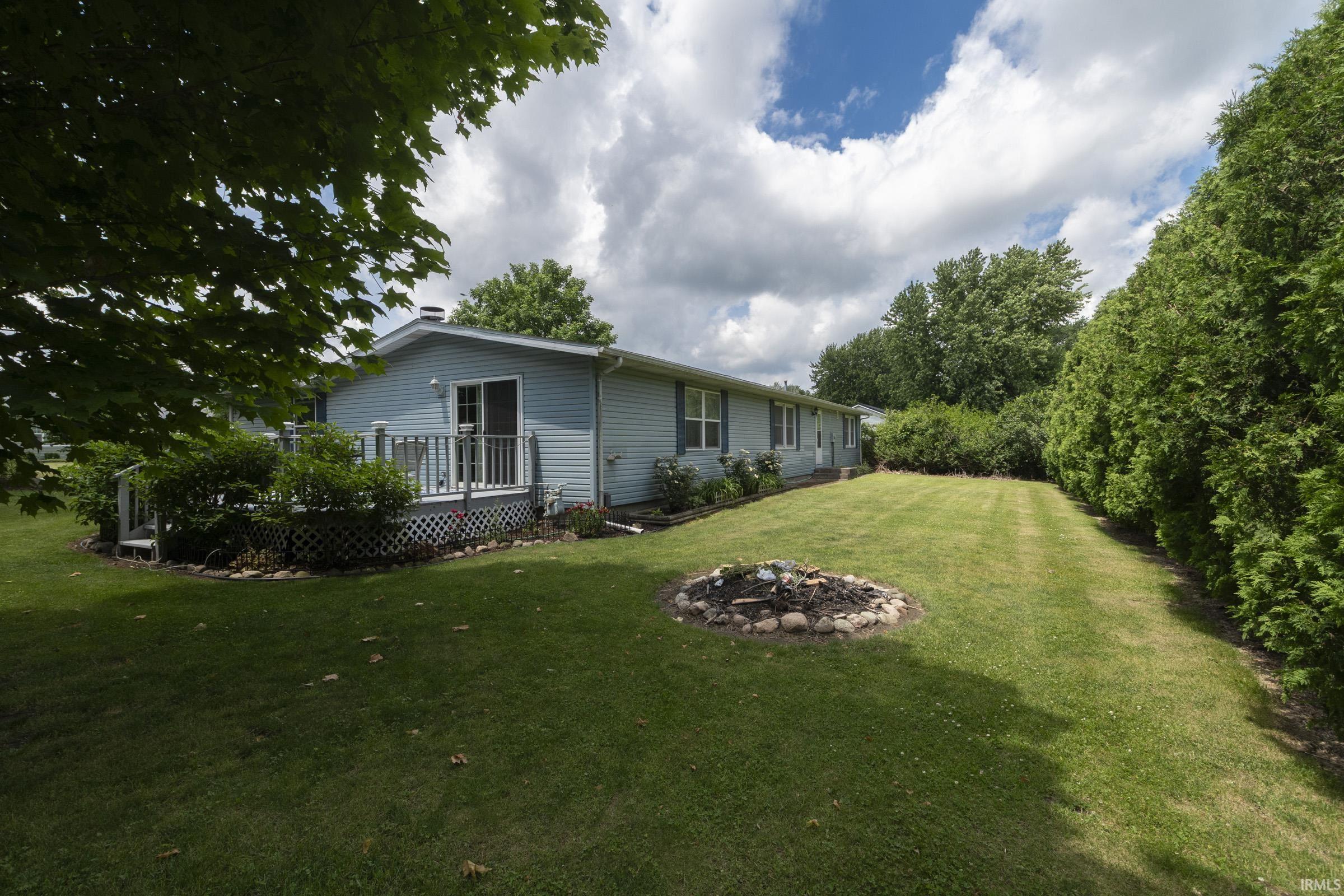 Expansive rear lawn with mature perimeter trees, a decorative stone-edged planter, and a light blue vinyl-sided exterior