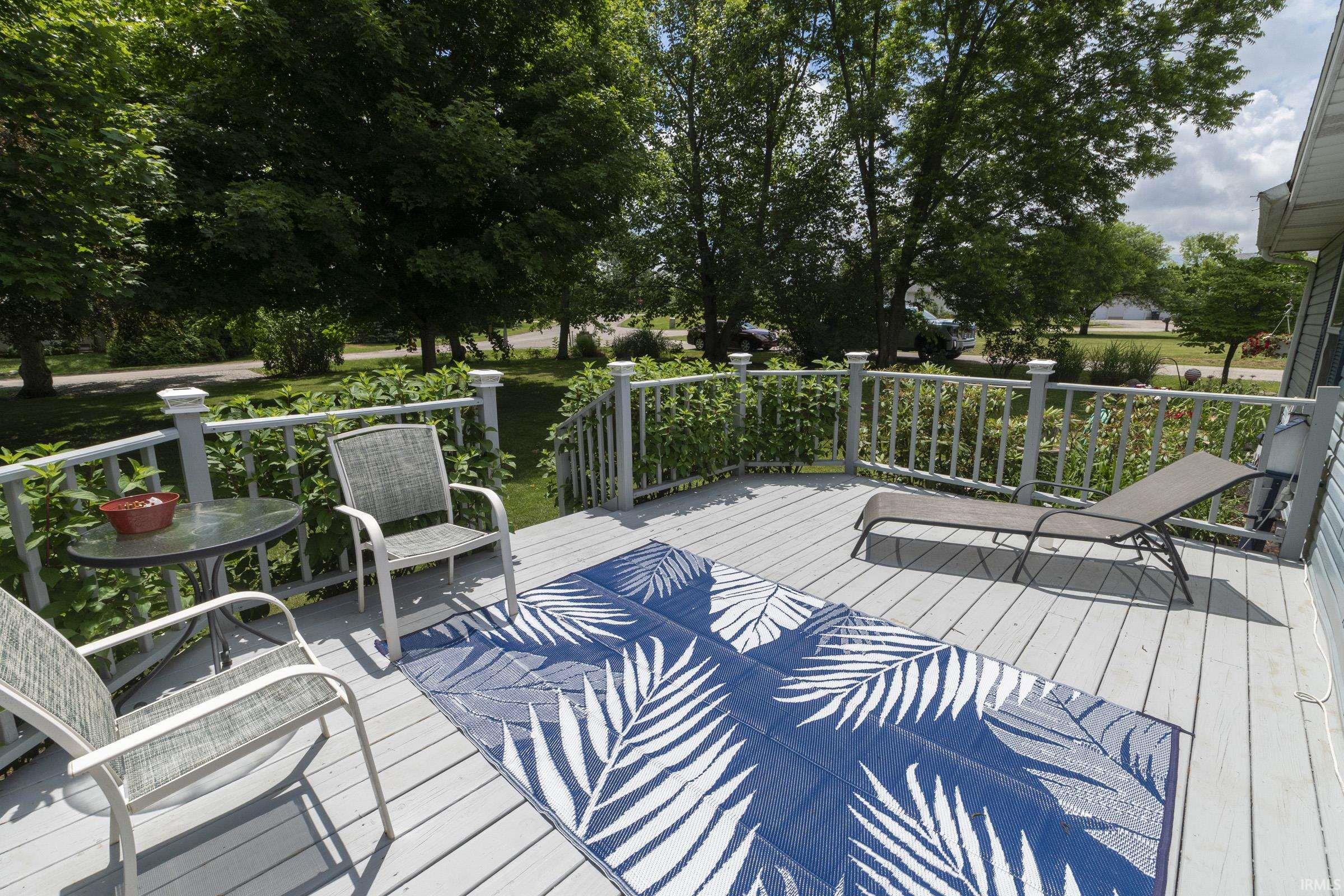 Spacious outdoor deck featuring gray wood-finish flooring, white railing with square posts, and mature surrounding greenery