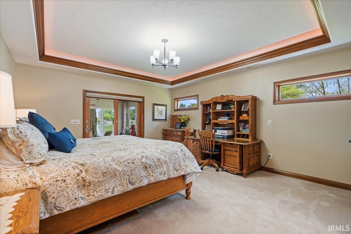 Spacious en-suite primary bedroom featuring a tray ceiling with wood trim, slider to 3 season room, recessed lighting, and carpet flooring